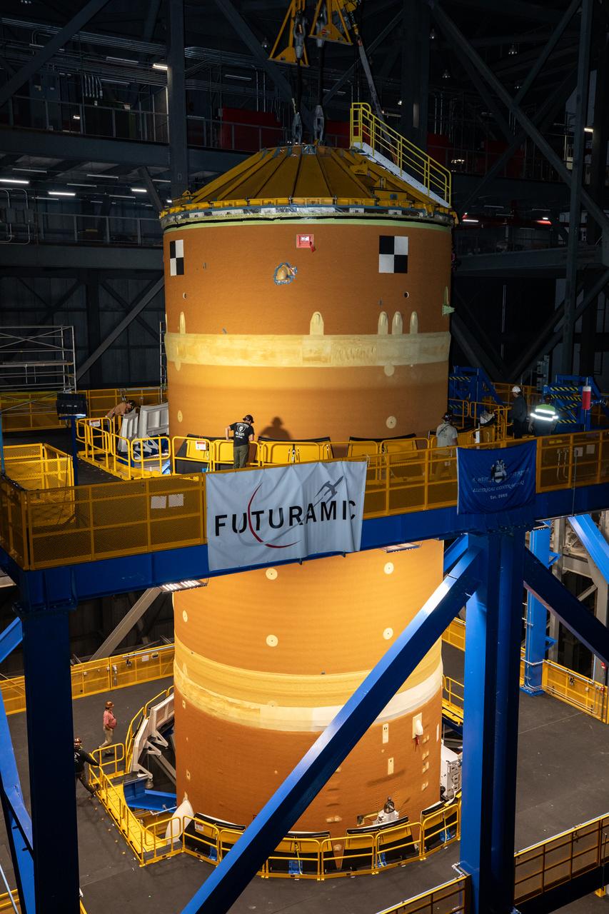 Teams with NASA’s Exploration Ground Systems transport lower the agency’s 212-foot-tall SLS (Space Launch System) core stage into High Bay 2 at the Vehicle Assembly Building at NASA’s Kennedy Space Center in Florida on Wednesday, Dec. 11, 2024. The one-of-a kind lifting beam is designed to lift the core stage from the transfer aisle to High Bay 2 where it will remain while teams stack the two solid rocket boosters on top of mobile launcher 1 for the SLS core stage. Boeing and their sub-contractor Futuramic refurbished High Bay 2 to increase efficiencies while processing core stages for Artemis II and beyond.