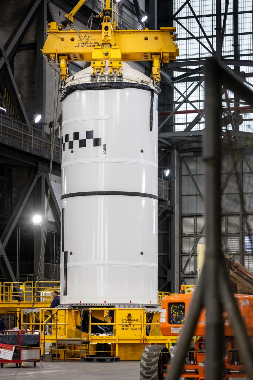 Technicians with NASA’s Exploration Ground Systems use a crane in the transfer aisle of the Vehicle Assembly Building at the agency’s Kennedy Space Center in Florida to prepare to lift the left forward segment for NASA’s SLS (Space Launch System) Moon rocket boosters on Wednesday, Feb. 5, 2025. The left forward segment will be transferred into High Bay 3 where it will be attached to the center forward segment on mobile launcher 1. The twin solid boosters, five segments on each side, will help support the remaining rocket components and the Orion spacecraft during final assembly of the Artemis II Moon rocket and provide more than 75 percent of the total SLS thrust during liftoff from NASA Kennedy’s Launch Pad 39B.