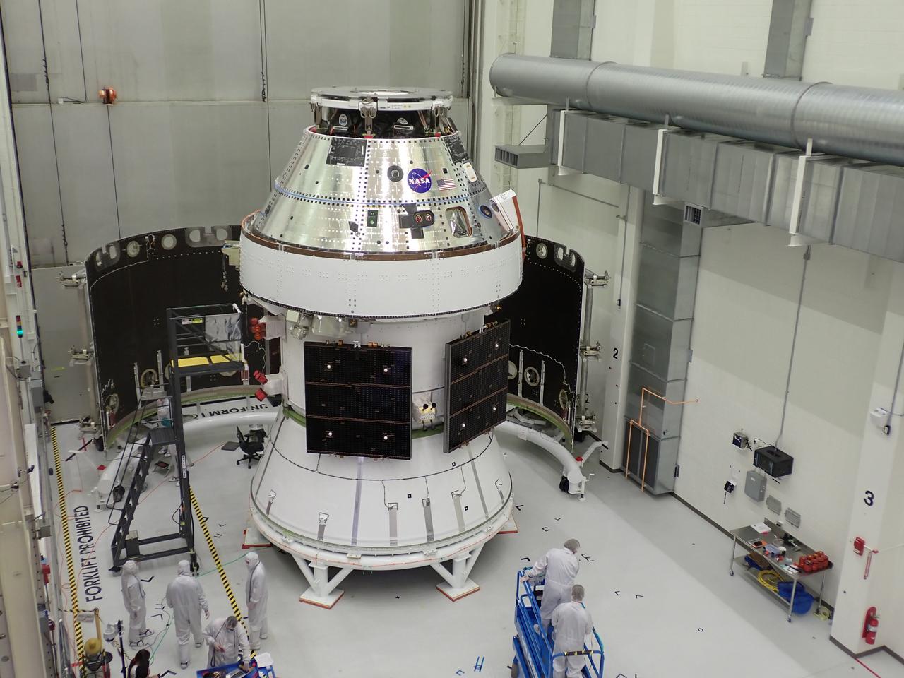 Technicians with Lockheed Martin prepare the Artemis II Orion spacecraft for the installation of three spacecraft adapter jettison fairings inside the Neil A. Armstrong Operations and Checkout Building at NASA’s Kennedy Space Center in Florida in on Tuesday, March 11, 2025. The fairings encapsulate the service module and protect the solar array wings, shielding them from the heat, wind, and acoustics of launch and ascent, plus help redistribute the load between Orion and the massive thrust of the SLS (Space Launch System) rocket during liftoff and ascent. Once the spacecraft is above the atmosphere, the three fairing panels will separate from the service module reducing the mass of the spacecraft. 