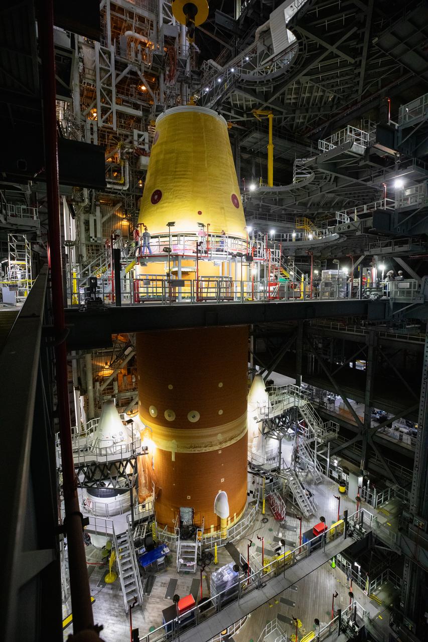 A massive crane lowers the launch vehicle stage adapter onto the SLS (Space Launch System) core stage on Thursday, April 3, 2025, in High Bay 3 inside the Vehicle Assembly Building at NASA’s Kennedy Space Center in Florida. During launch and ascent, the launch vehicle stage adapter provides structural support and protects avionics and electrical devices within the upper stage from extreme vibrations and acoustic conditions. The Artemis II test flight will take a crew of four astronauts on a 10-day journey around the Moon, helping confirm the foundational systems and hardware needed for human deep space exploration. 