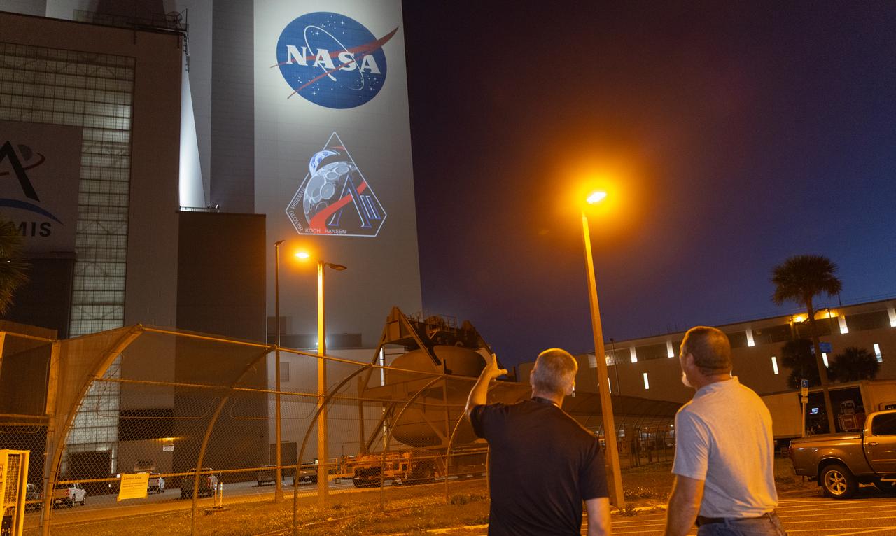 Employees at NASA’s Kennedy Space Center in Florida take photos of the official Artemis II mission crew insignia projected on the exterior of the spaceport’s Vehicle Assembly Building on Friday, April 4, 2025. The patch designates the mission as “AII,” signifying not only the second major flight of the Artemis campaign, but also an endeavor of discovery that seeks to explore for all and by all. Framed in Apollo 8’s famous Earthrise photo, the scene of the Earth and the Moon represents the dual nature of human spaceflight, both equally compelling: The Moon represents our exploration destination, focused on discovery of the unknown. The Earth represents home, focused on the perspective we gain when we look back at our shared planet and learn what it is to be uniquely human. The orbit around Earth highlights the ongoing exploration missions that have enabled Artemis to set sights on a long-term presence on the Moon and soon, Mars.