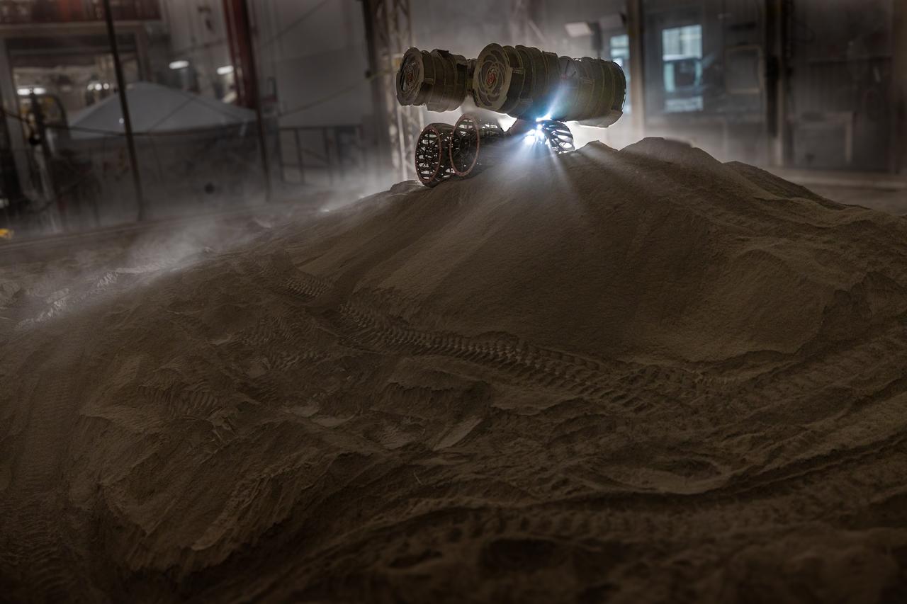 NASA’s RASSOR (Regolith Advanced Surface Systems Operations Robot) manipulates simulated regolith, or lunar dust found on the Moon’s surface, to create a three-foot berm during a site preparation test inside of the Granular Mechanics and Regolith Operations Lab at the agency’s Kennedy Space Center in Florida on Tuesday, June 3, 2025. The opposing motion of the bucket drums helps RASSOR grip the surface in low-gravity environments like the Moon or Mars. With this unique capability, RASSOR can traverse the rough surface to dig, load, haul, and dump regolith that could be used in construction or broken down into hydrogen, oxygen, or water, resources critical for sustaining human presence. RASSOR represents an earlier generation technology that informed the development of NASA’s IPEx (In-Situ Resource Utilization Pilot Excavator), serving as a precursor and foundational platform for the advanced excavation systems and autonomous capabilities now being demonstrated by this Moon-mining robot.