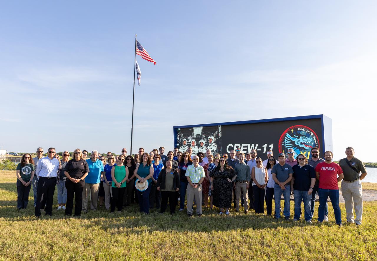 NASA’s Commercial Crew Program employees pose for a photo following the raising of the agency’s SpaceX Crew-11 mission flag near the countdown clock at the NASA News Center at the agency’s Kennedy Space Center in Florida on Wednesday, July 30, 2025. The Crew-11 mission will send NASA astronauts Zena Cardman and Mike Fincke, along with JAXA (Japan Aerospace Exploration Agency) astronaut Kimiya Yui and Roscosmos cosmonaut Oleg Platonov to the International Space Station aboard SpaceX’s Dragon spacecraft and Falcon 9 at 12:09 p.m. EDT on Thursday, July 31, 2025, from NASA Kennedy’s Launch Complex 39A.  