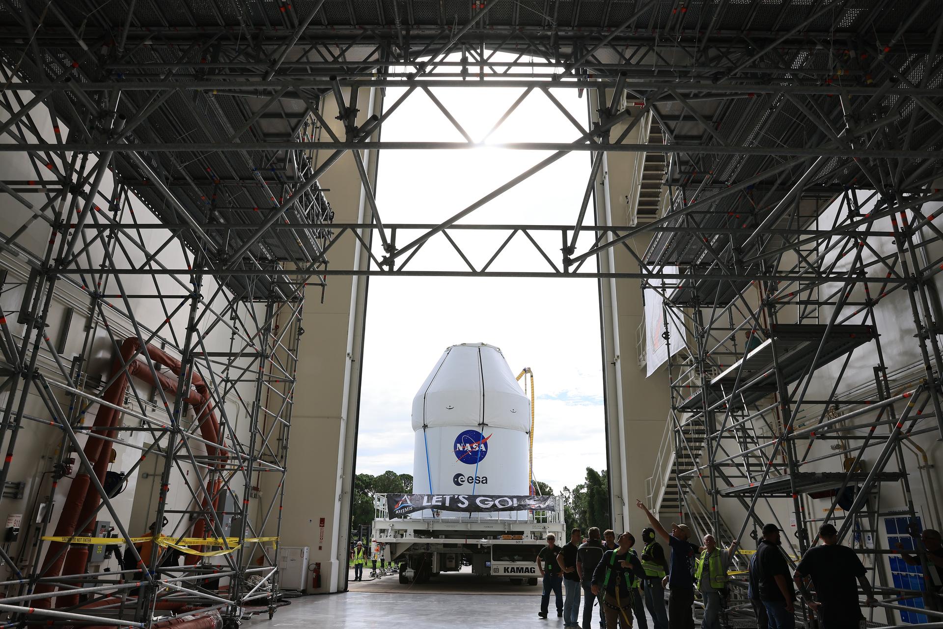 Image shows a white structure with NASA insignia on a semi-trailer approaching a building