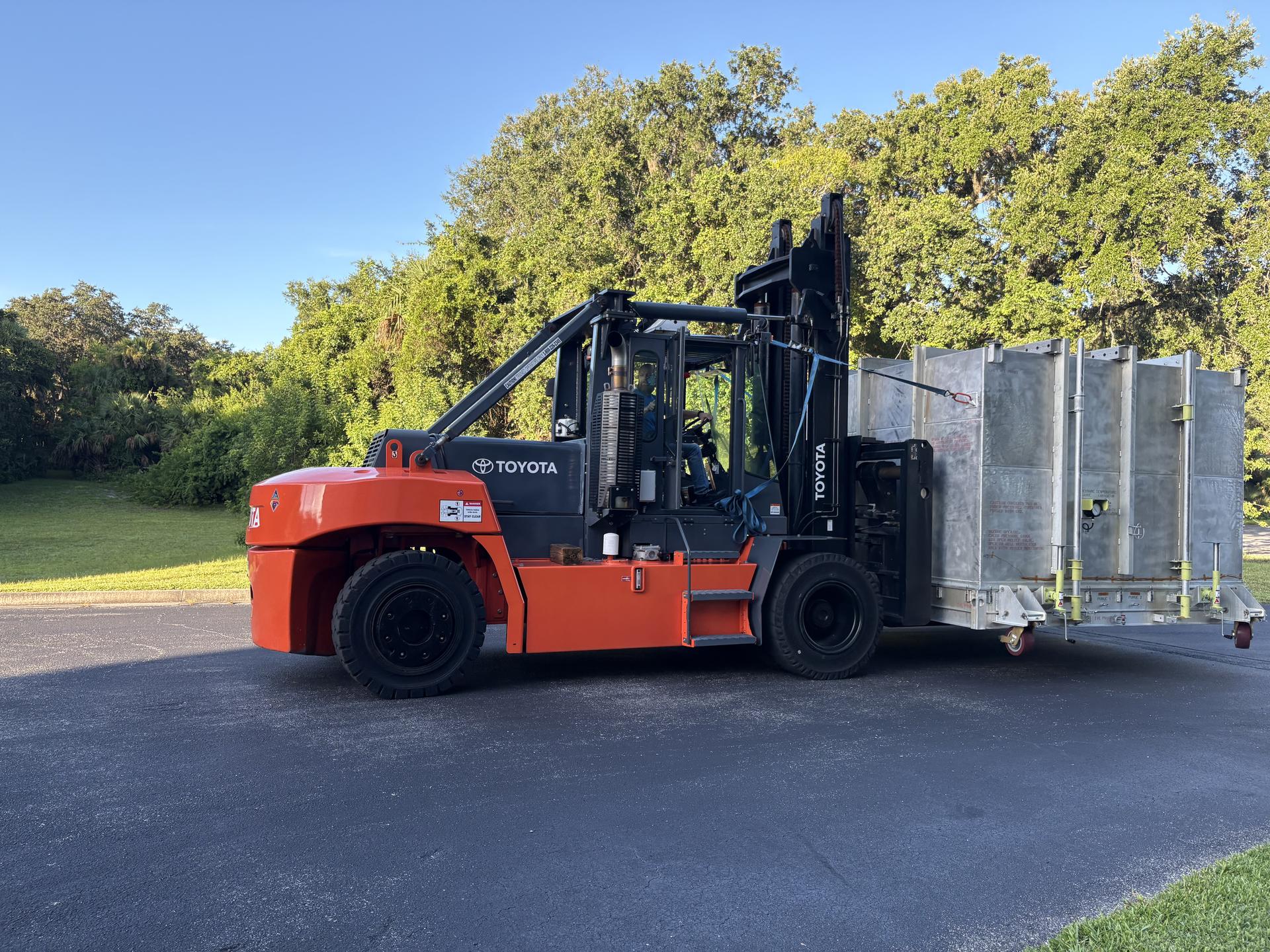 Image shows a forklift vehicle carrying a rectangle box with NASA's IMAP mission inside.