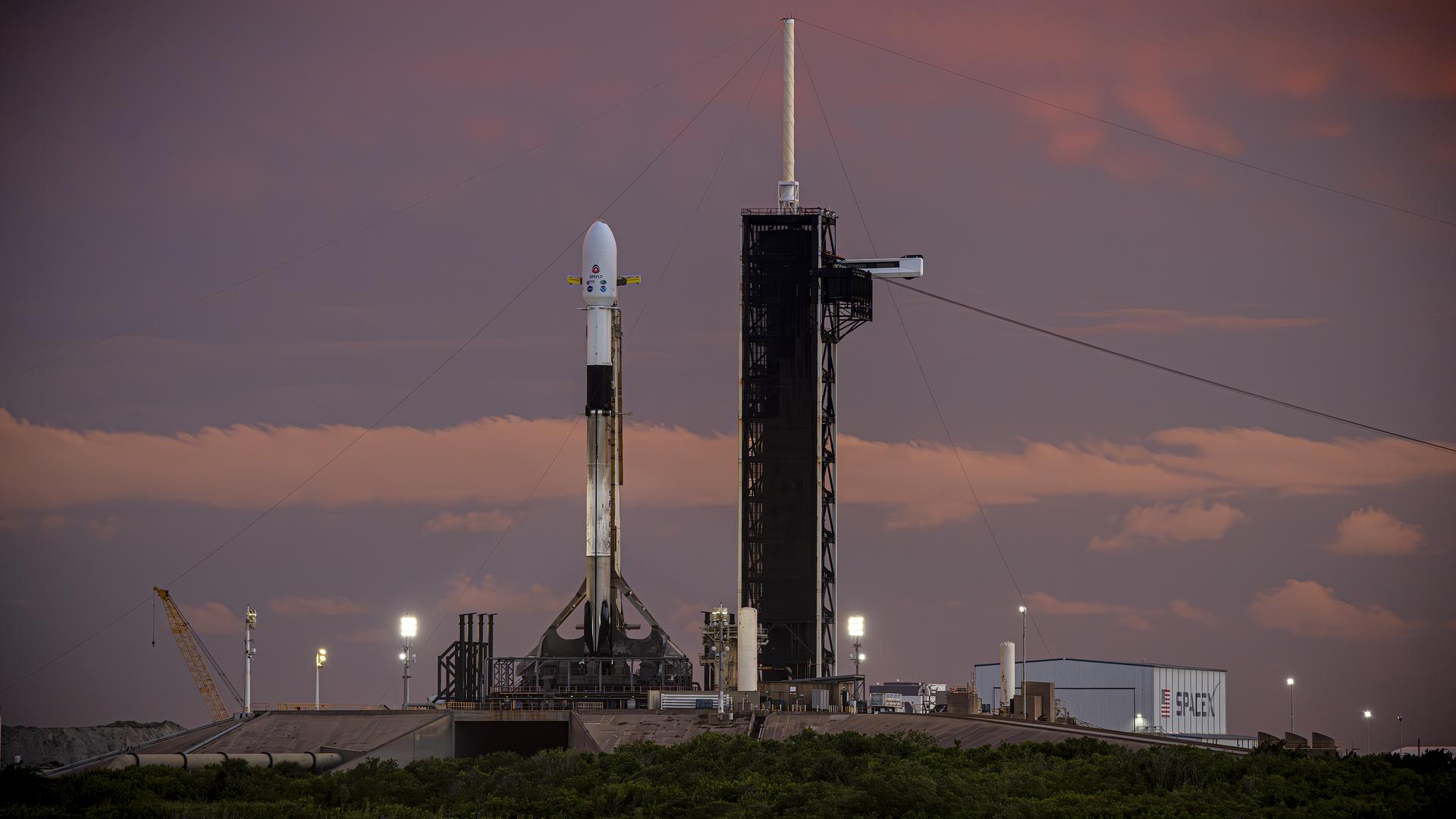 Image shows a SpaceX rocket at the launch pad carrying NASA's IMAP observatory, NASA's Carruthers Geocorona Observatory, and NOAA's SWFO-L1 satellite