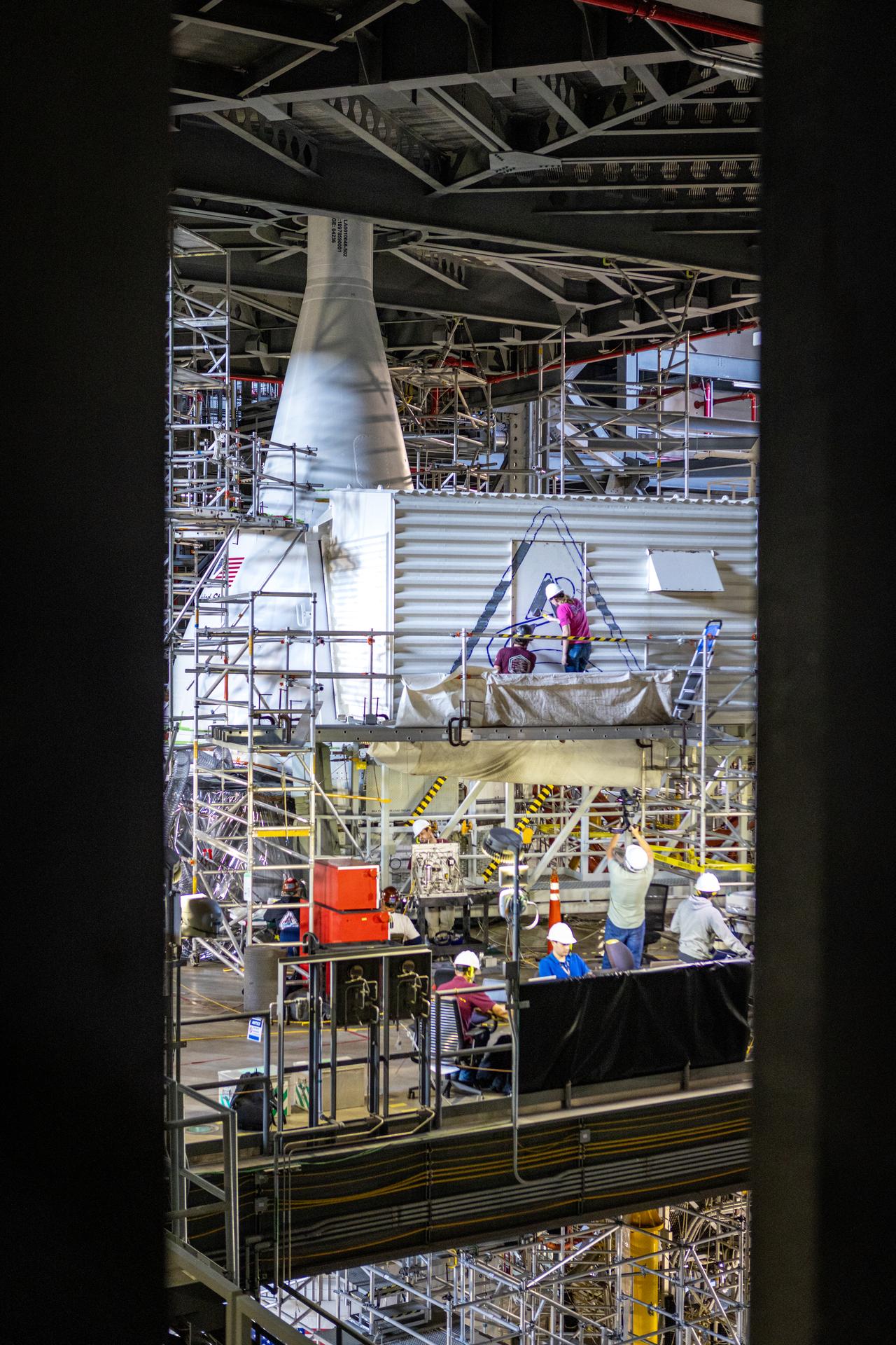 From left, Sean McCrary and Katie Mortensen, mechanical engineering technicians, paint NASA’s Artemis logo on the White Room connected to the crew access arm and mobile launcher inside the Vehicle Assembly Building at NASA’s Kennedy Space Center in Florida on Thursday, Dec. 4, 2025. The White Room is the area where the Artemis II crew Reid Wiseman, Victor Glover, Christina Koch, and CSA (Canadian Space Agency) astronaut Jeremy Hansen will enter the Orion spacecraft ahead of launch from Launch Complex 39B at NASA Kennedy in early 2026.