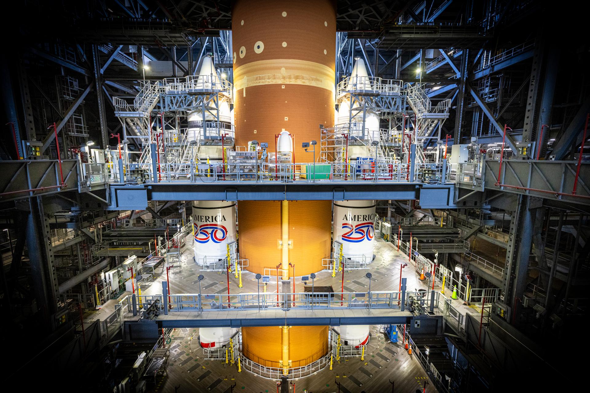 Technicians with NASA’s Exploration Ground Systems Program complete installation of the America 250 emblem on the twin SLS (Space Launch System) solid rocket boosters for the Artemis II mission inside the Vehicle Assembly Building at NASA’s Kennedy Space Center in Florida on Thursday, Dec. 4, 2025. The SLS rocket and the Orion spacecraft will carry NASA astronauts Reid Wiseman, Victor Glover, Christina Koch, and CSA (Canadian Space Agency) astronaut Jeremy Hansen on a 10-day mission around the Moon and back in early 2026 from Launch Complex 39B at NASA Kennedy. America 250 commemorates the 250th anniversary of the signing of the Declaration of Independence with NASA celebrating the “Spirit of Innovation” theme to inspire future generations.