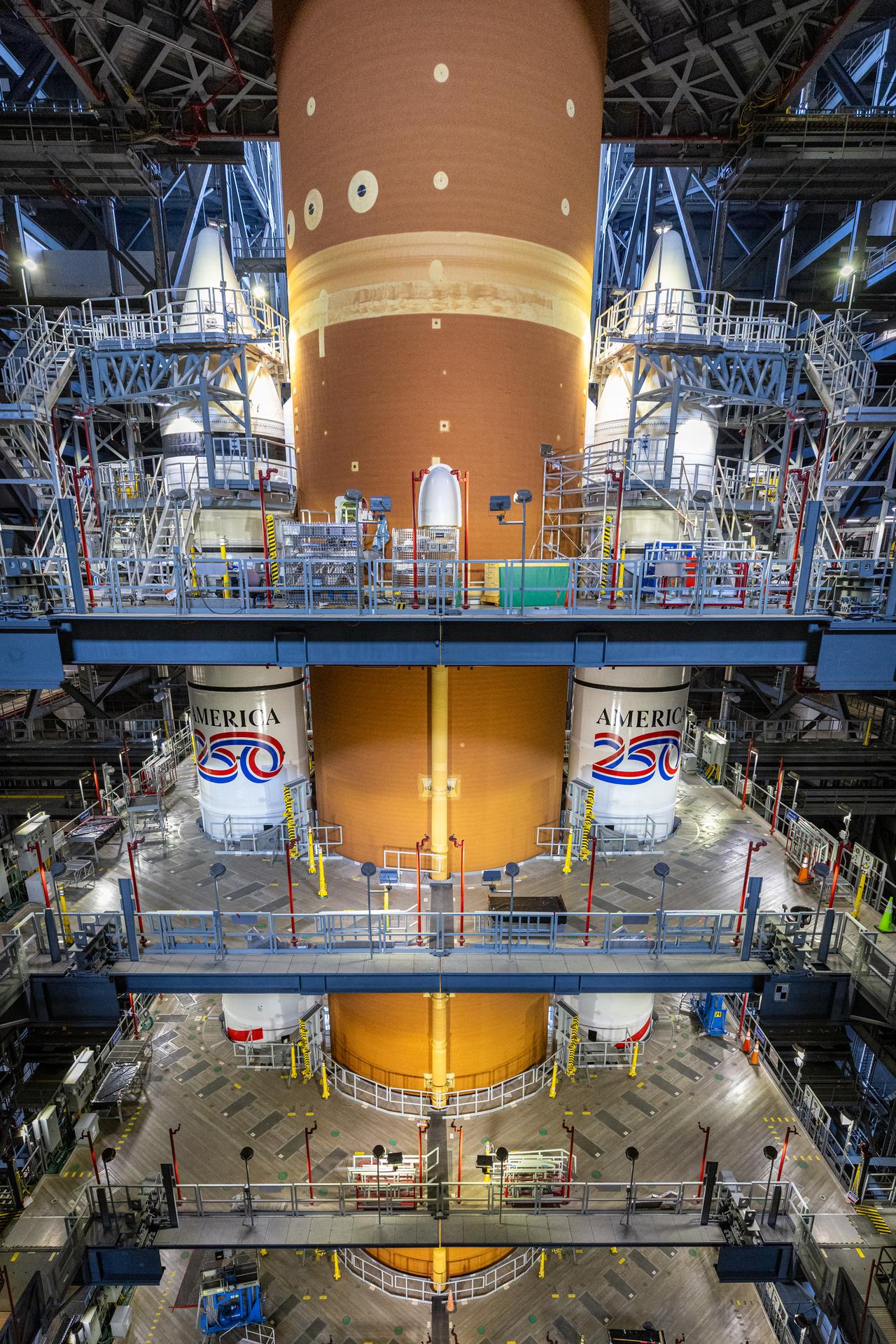 Technicians with NASA’s Exploration Ground Systems Program complete installation of the America 250 emblem on the twin SLS (Space Launch System) solid rocket boosters for the Artemis II mission inside the Vehicle Assembly Building at NASA’s Kennedy Space Center in Florida on Thursday, Dec. 4, 2025. The SLS rocket and the Orion spacecraft will carry NASA astronauts Reid Wiseman, Victor Glover, Christina Koch, and CSA (Canadian Space Agency) astronaut Jeremy Hansen on a 10-day mission around the Moon and back in early 2026 from Launch Complex 39B at NASA Kennedy. America 250 commemorates the 250th anniversary of the signing of the Declaration of Independence with NASA celebrating the “Spirit of Innovation” theme to inspire future generations.