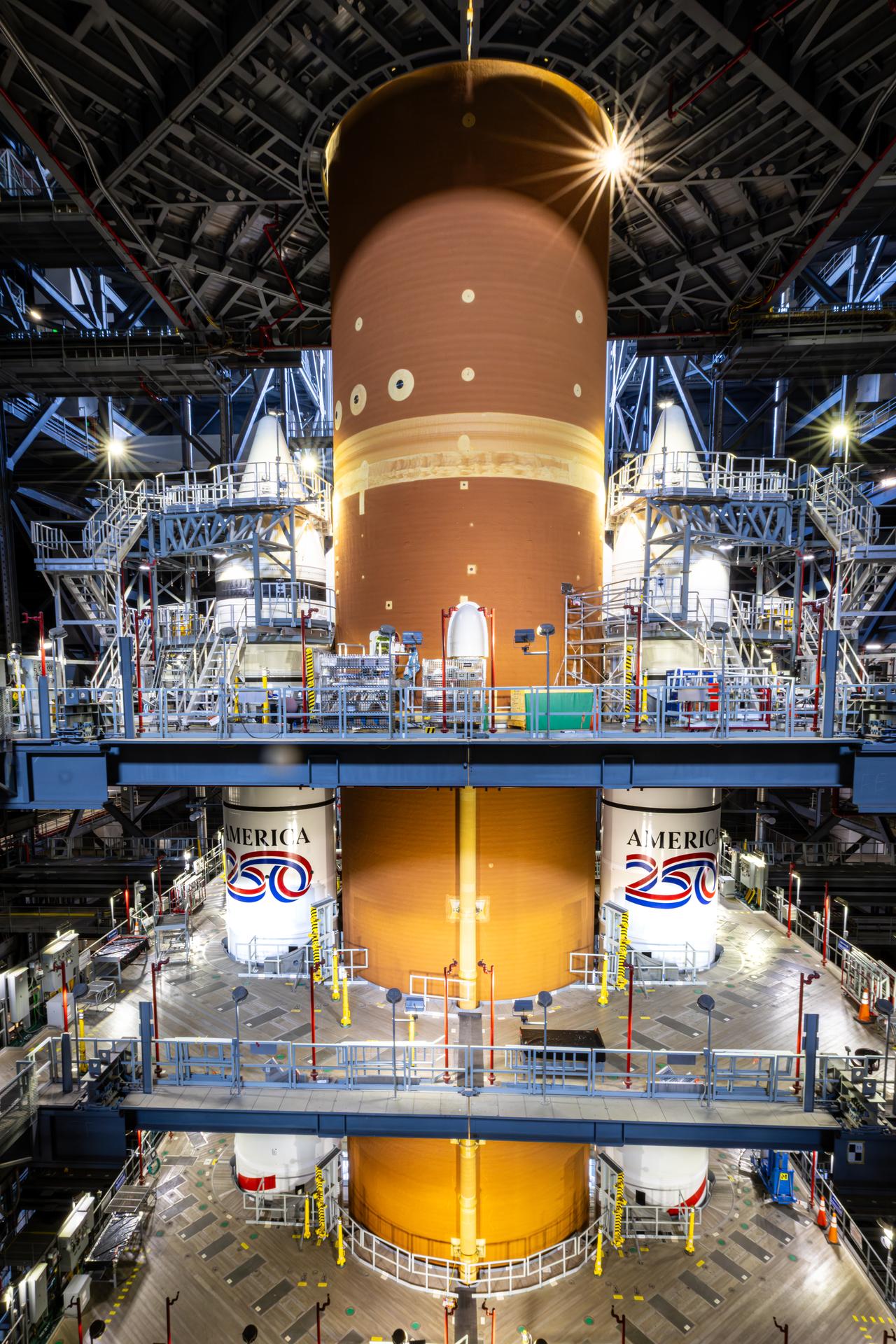 Technicians with NASA’s Exploration Ground Systems Program complete installation of the America 250 emblem on the twin SLS (Space Launch System) solid rocket boosters for the Artemis II mission inside the Vehicle Assembly Building at NASA’s Kennedy Space Center in Florida on Thursday, Dec. 4, 2025. The SLS rocket and the Orion spacecraft will carry NASA astronauts Reid Wiseman, Victor Glover, Christina Koch, and CSA (Canadian Space Agency) astronaut Jeremy Hansen on a 10-day mission around the Moon and back in early 2026 from Launch Complex 39B at NASA Kennedy. America 250 commemorates the 250th anniversary of the signing of the Declaration of Independence with NASA celebrating the “Spirit of Innovation” theme to inspire future generations.