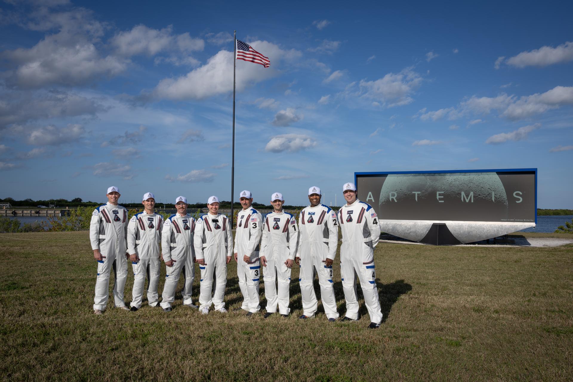 Members of the Artemis II closeout crew, from left, William Sattler; Tyler Sutherland; Michael Heinemann; Jenni Gibbons, Artemis II backup crew member; Bill Owens; Taylor Hose; Andre Douglas, Artemis II backup crew member; and Christian Warriner pose for a photo near the countdown clock featuring the Artemis Moon logo at the NASA News Center at the agency’s Kennedy Space Center in Florida on Thursday, Dec. 19, 2025. The closeout crew is responsible for safely securing the astronauts inside the Orion spacecraft on launch day and closing the hatch during launch countdown. 