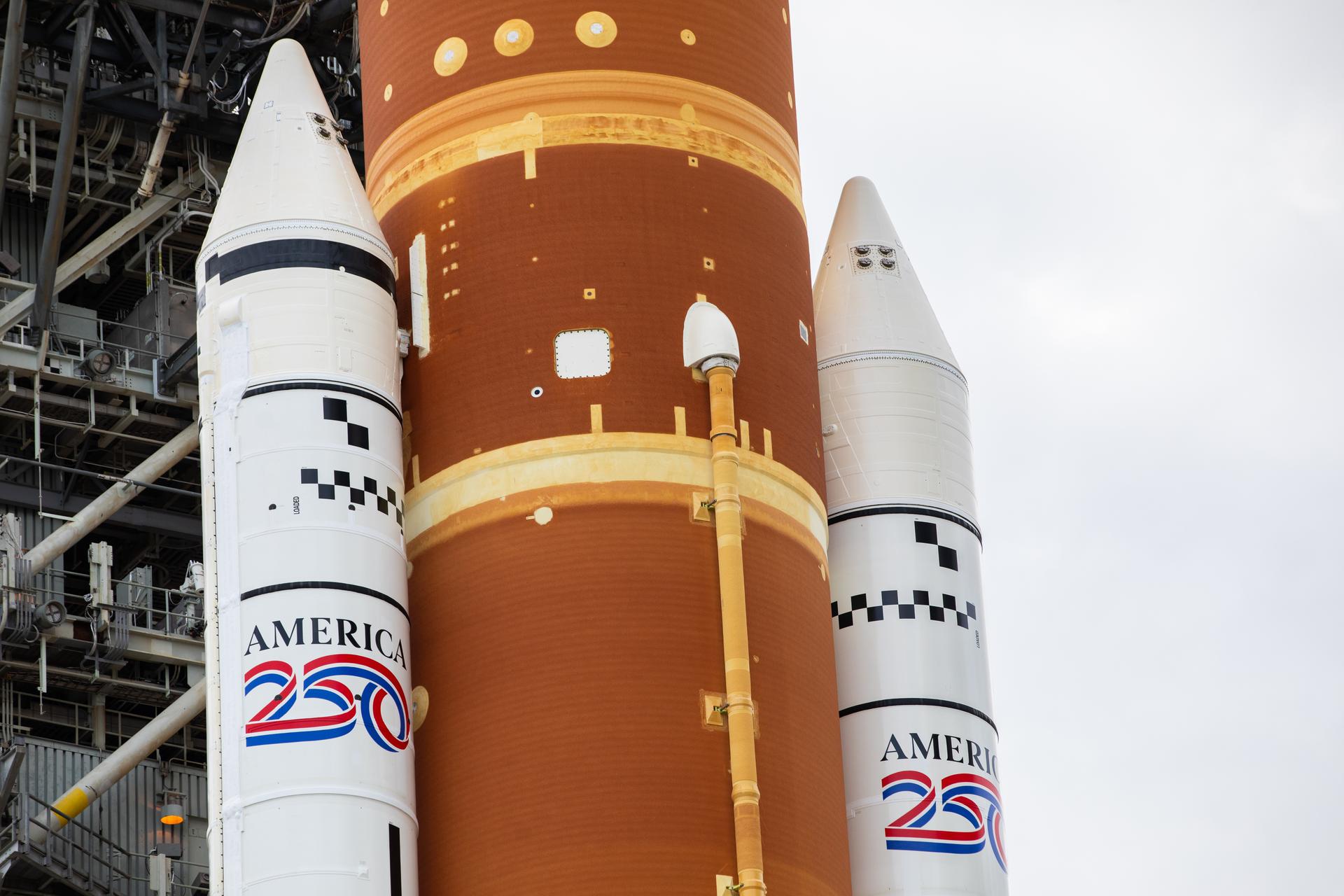 The America 250 logo is displayed on the twin SLS (Space Launch System) solid rocket boosters during rollout of NASA’s Artemis II SLS and Orion spacecraft from the Vehicle Assembly Building to Launch Complex 39B at NASA’s Kennedy Space Center in Florida on Saturday, Jan. 17, 2026. The Artemis II test flight will take Commander Reid Wiseman, Pilot Victor Glover, and Mission Specialist Christina Koch from NASA, and Mission Specialist Jeremy Hansen from the CSA (Canadian Space Agency), around the Moon and back to Earth no later than April 2026. 