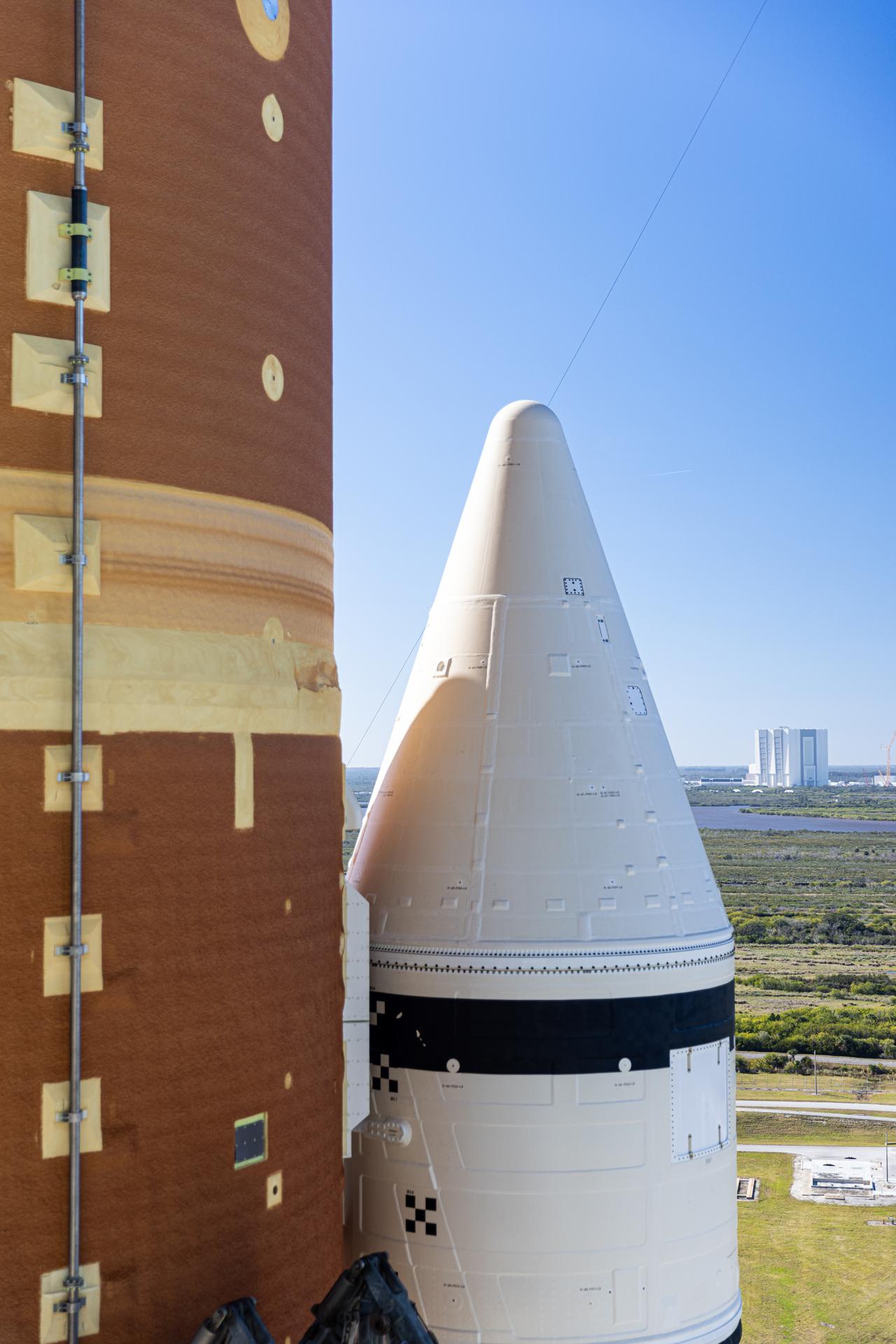 This photograph shows a closeup view of one of the solid rocket boosters attached to NASA’s Artemis II SLS (Space Launch System) rocket at Launch Complex 39B with the Vehicle Assembly Building in the background at NASA’s Kennedy Space Center in Florida on Tuesday, Jan. 20, 2026. The Artemis II test flight will take Commander Reid Wiseman, Pilot Victor Glover, and Mission Specialist Christina Koch from NASA, and Mission Specialist Jeremy Hansen from the CSA (Canadian Space Agency), on a 10-day journey no earlier than 6:24 p.m. EDT on Wednesday, April 1. 
