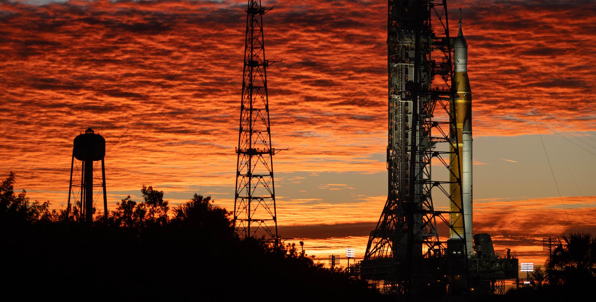 Clouds and the Sun illuminate the sky on Wednesday, Jan. 28, 2026, as NASA’s Artemis II SLS (Space Launch System) rocket and Orion spacecraft stand vertical at Launch Complex 39B at NASA’s Kennedy Space Center in Florida. The Artemis II test flight will take Commander Reid Wiseman, Pilot Victor Glover, and Mission Specialist Christina Koch from NASA and Mission Specialist Jeremy Hansen from the CSA (Canadian Space Agency), around the Moon and back to Earth no later than April 2026.