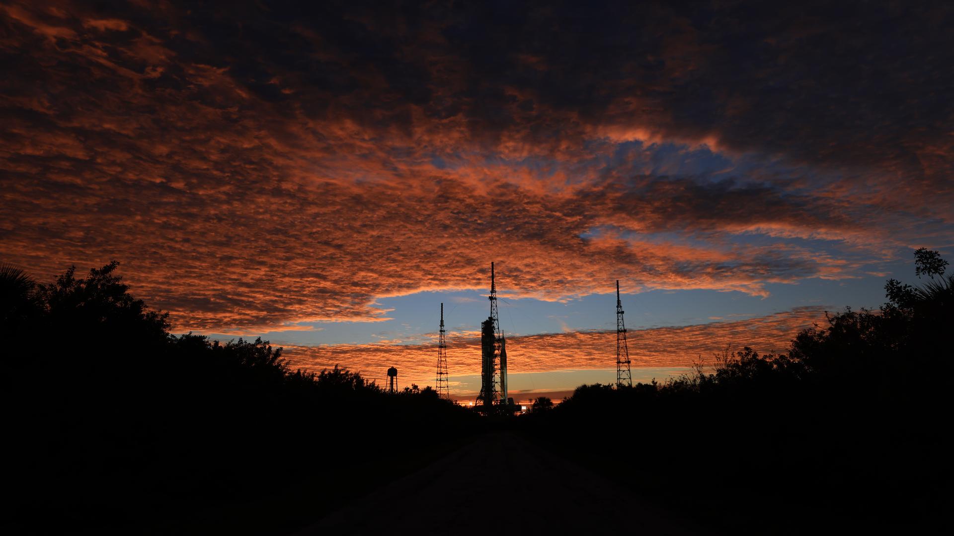 Clouds and the Sun illuminate the sky on Wednesday, Jan. 28, 2026, as NASA’s Artemis II SLS (Space Launch System) rocket and Orion spacecraft stand vertical at Launch Complex 39B at NASA’s Kennedy Space Center in Florida. The Artemis II test flight will take Commander Reid Wiseman, Pilot Victor Glover, and Mission Specialist Christina Koch from NASA and Mission Specialist Jeremy Hansen from the CSA (Canadian Space Agency), around the Moon and back to Earth no later than April 2026.