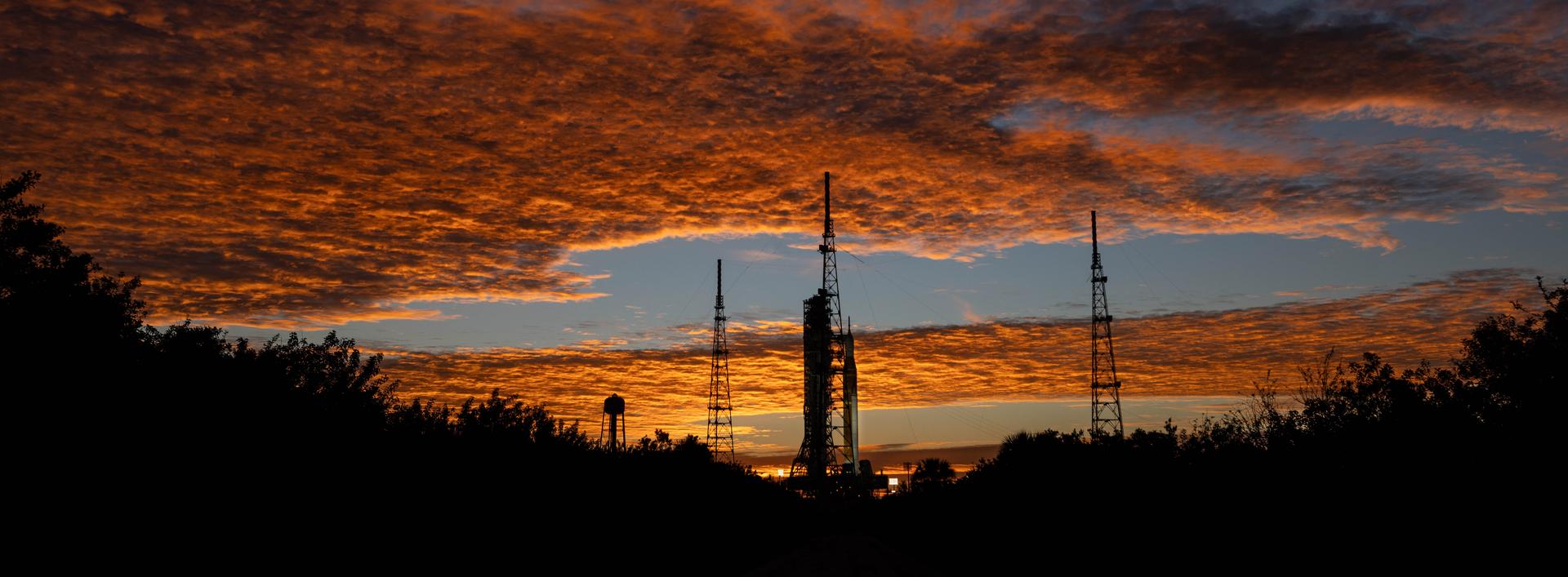 Clouds and the Sun illuminate the sky on Wednesday, Jan. 28, 2026, as NASA’s Artemis II SLS (Space Launch System) rocket and Orion spacecraft stand vertical at Launch Complex 39B at NASA’s Kennedy Space Center in Florida. The Artemis II test flight will take Commander Reid Wiseman, Pilot Victor Glover, and Mission Specialist Christina Koch from NASA and Mission Specialist Jeremy Hansen from the CSA (Canadian Space Agency), around the Moon and back to Earth no later than April 2026.