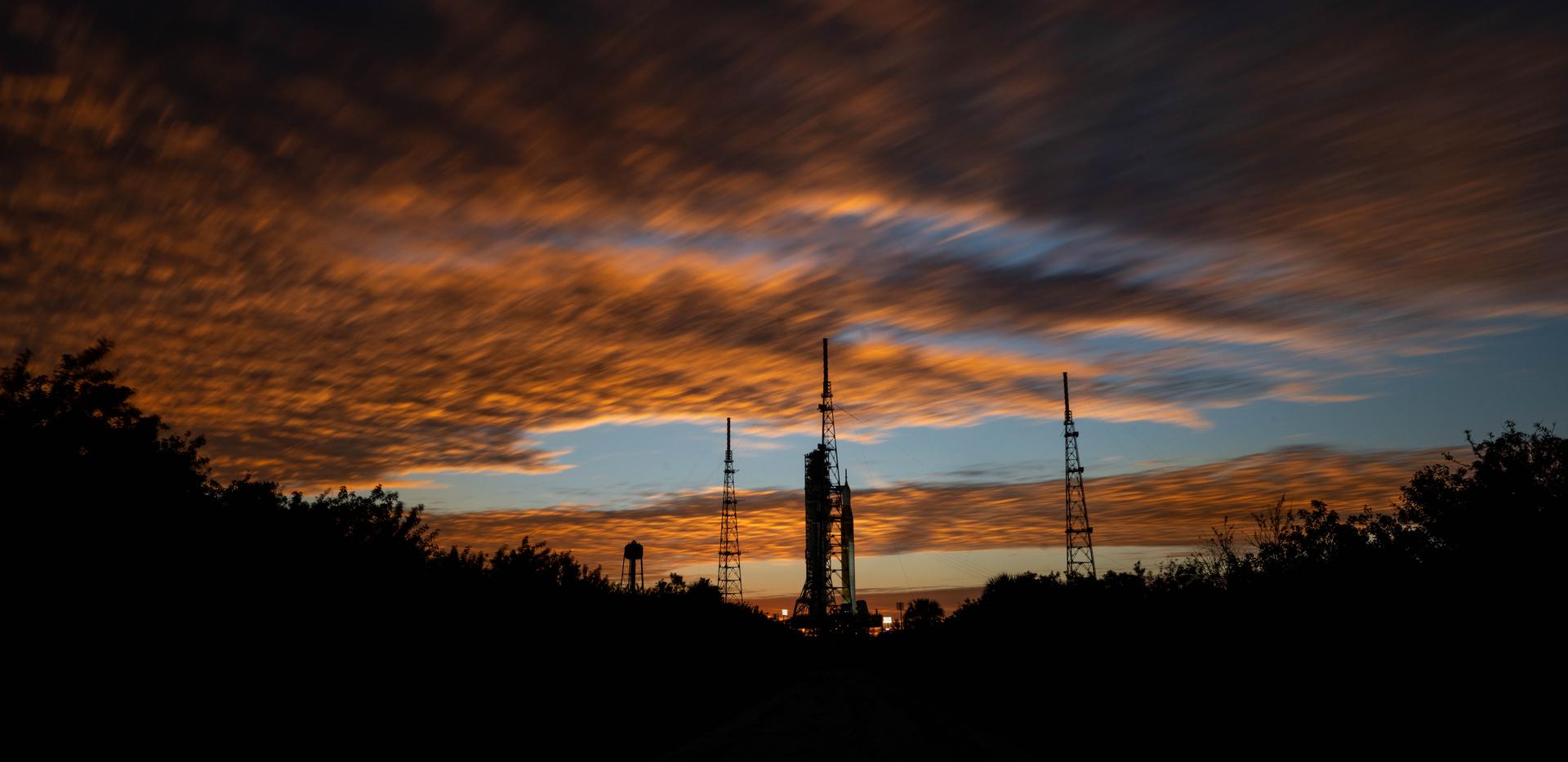 Clouds and the Sun illuminate the sky on Wednesday, Jan. 28, 2026, as NASA’s Artemis II SLS (Space Launch System) rocket and Orion spacecraft stand vertical at Launch Complex 39B at NASA’s Kennedy Space Center in Florida. The Artemis II test flight will take Commander Reid Wiseman, Pilot Victor Glover, and Mission Specialist Christina Koch from NASA and Mission Specialist Jeremy Hansen from the CSA (Canadian Space Agency), around the Moon and back to Earth no later than April 2026.