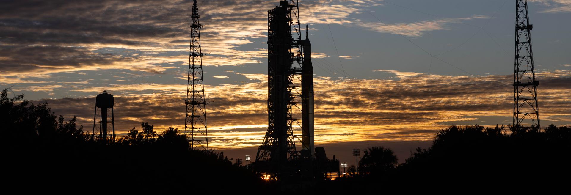 Clouds and the Sun illuminate the sky on Wednesday, Jan. 28, 2026, as NASA’s Artemis II SLS (Space Launch System) rocket and Orion spacecraft stand vertical at Launch Complex 39B at NASA’s Kennedy Space Center in Florida. The Artemis II test flight will take Commander Reid Wiseman, Pilot Victor Glover, and Mission Specialist Christina Koch from NASA and Mission Specialist Jeremy Hansen from the CSA (Canadian Space Agency), around the Moon and back to Earth no later than April 2026.