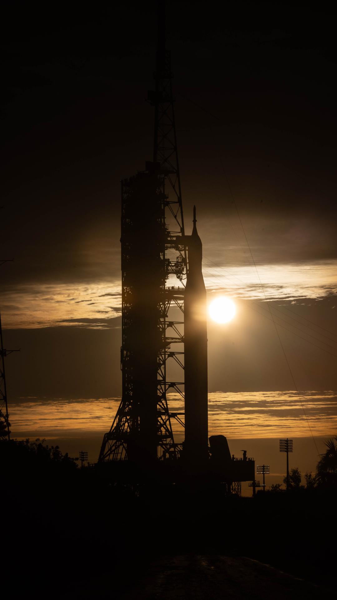 The sunrise peeks between NASA’s Artemis II SLS (Space Launch System) rocket with the Orion spacecraft atop and the mobile launcher at Launch Complex 39B at NASA’s Kennedy Space Center in Florida on Wednesday, Jan. 28, 2026. The Artemis II test flight will take Commander Reid Wiseman, Pilot Victor Glover, and Mission Specialist Christina Koch from NASA and Mission Specialist Jeremy Hansen from the CSA (Canadian Space Agency), around the Moon and back to Earth no later than April 2026.