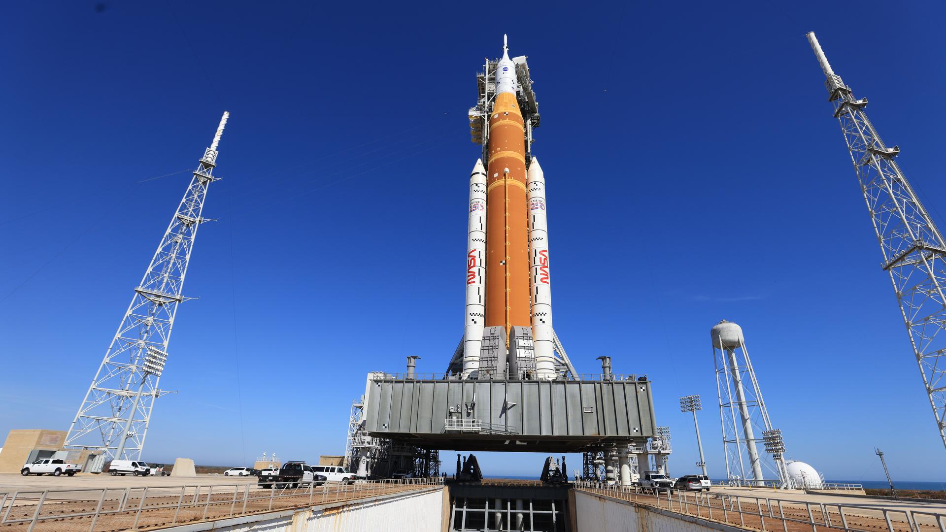 The Artemis II SLS rocket and Orion spacecraft at the launch pad under a blue sky.