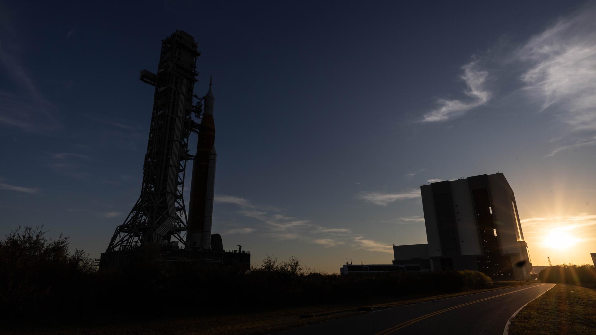 NASA’s crawler-transporter 2, carrying NASA’s Artemis II SLS (Space Launch System) rocket with the Orion spacecraft secured to mobile launcher 1, approaches the Vehicle Assembly Building at NASA’s Kennedy Space Center in Florida as the sun sets on Wednesday, Feb. 25, 2026, to troubleshoot the flow of helium to the rocket’s upper stage, the interim cryogenic propulsion stage. Seen in the background is also mobile launcher 2, which will be used on future Artemis flights beginning with Artemis IV. Once complete, the SLS rocket will roll back to Launch Complex 39B to prepare to launch four astronauts around the Moon and back for the Artemis II test flight. 