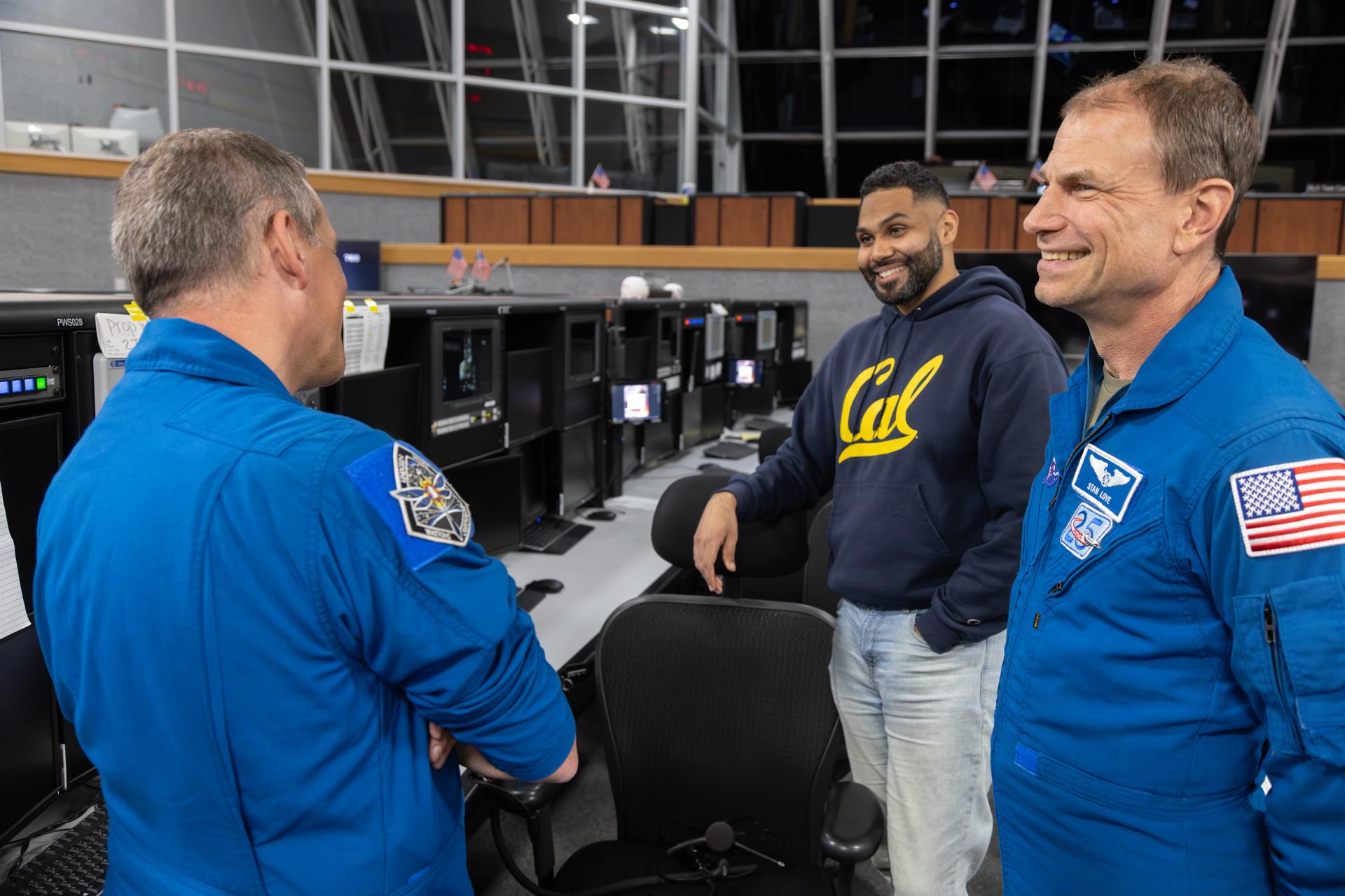 From left, NASA astronauts Bob Hines and Stan Love talk with Mike Guzman, Artemis launch team member, inside Firing Room 1 of the Rocco A. Petrone Launch Control Center during the Artemis II rollout of the SLS (Space Launch System) rocket and Orion spacecraft from the Vehicle Assembly Building to Launch Complex 39B at NASA’s Kennedy Space Center in Florida on Friday, March, 20, 2026. The Artemis II test flight will take Commander Reid Wiseman, Pilot Victor Glover, and Mission Specialist Christina Koch from NASA, and Mission Specialist Jeremy Hansen from the CSA (Canadian Space Agency), around the Moon and back to Earth with launch opportunities beginning in April 2026.