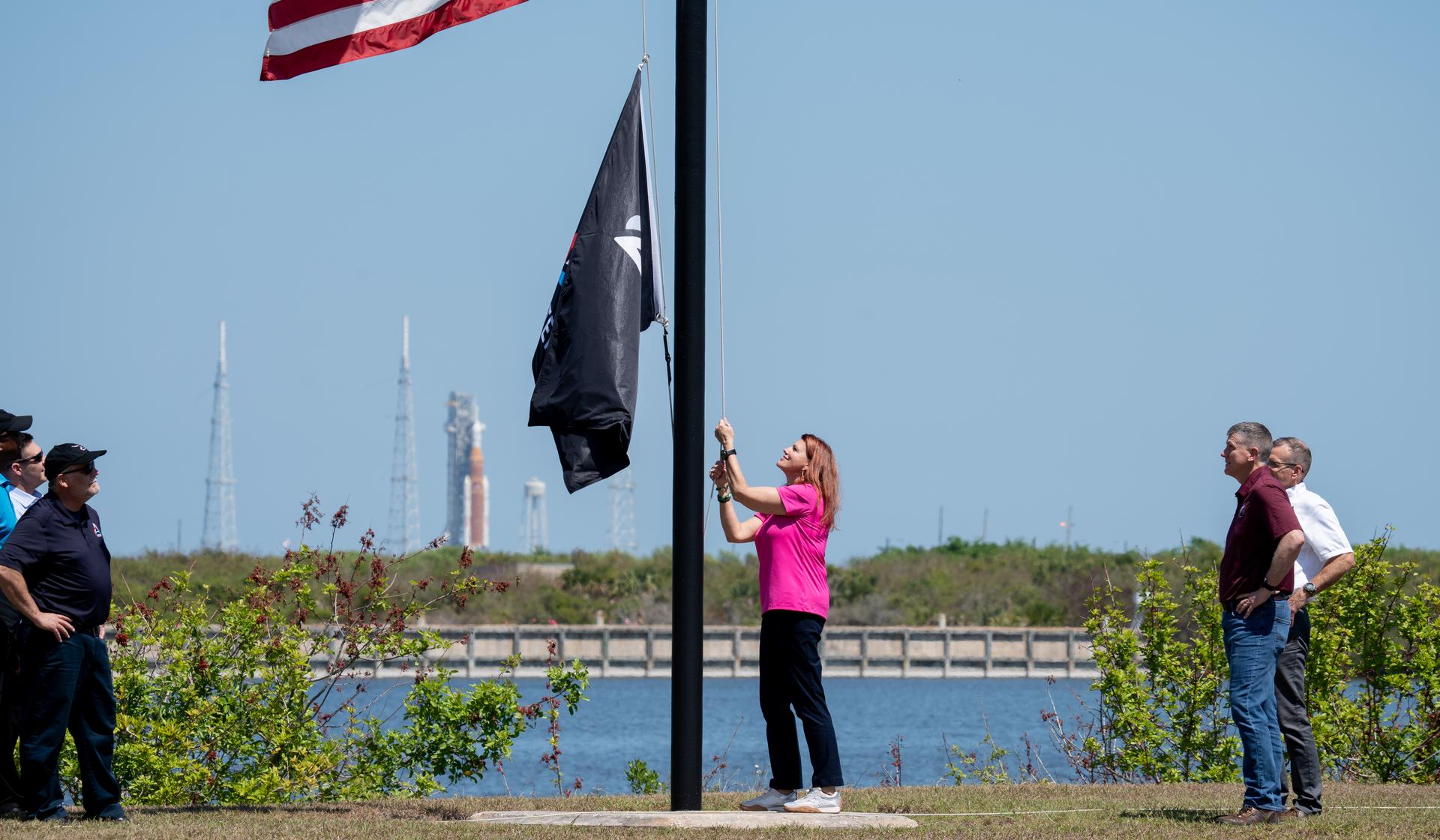 From left, NASA Kennedy Space Center Deputy Director Kelvin Manning; Robert Yaskovic, associate manager, Exploration Ground Systems Program; Shawn Quinn, manager, Exploration Ground Systems Program; Charlie Blackwell-Thompson, Artemis II launch director; Cliff Lanham, deputy manager, Exploration Ground Systems Program; and Jeremy Graeber, assistant launch director, Exploration Ground Systems Program raise the Artemis flag near the countdown clock at the NASA News Center at NASA’s Kennedy Space Center in Florida on Friday, March 27, 2026.  The Artemis II test flight mission will take Artemis II Commander Reid Wiseman, Pilot Victor Glover, and Mission Specialist Christina Koch from NASA, and Mission Specialist Jeremy Hansen from the CSA (Canadian Space Agency) on a 10-day journey around the Moon and back aboard NASA’s SLS (Space Launch System) rocket and Orion spacecraft from Launch Complex 39B no earlier than 6:24 p.m. EDT on Wednesday, April 1. 