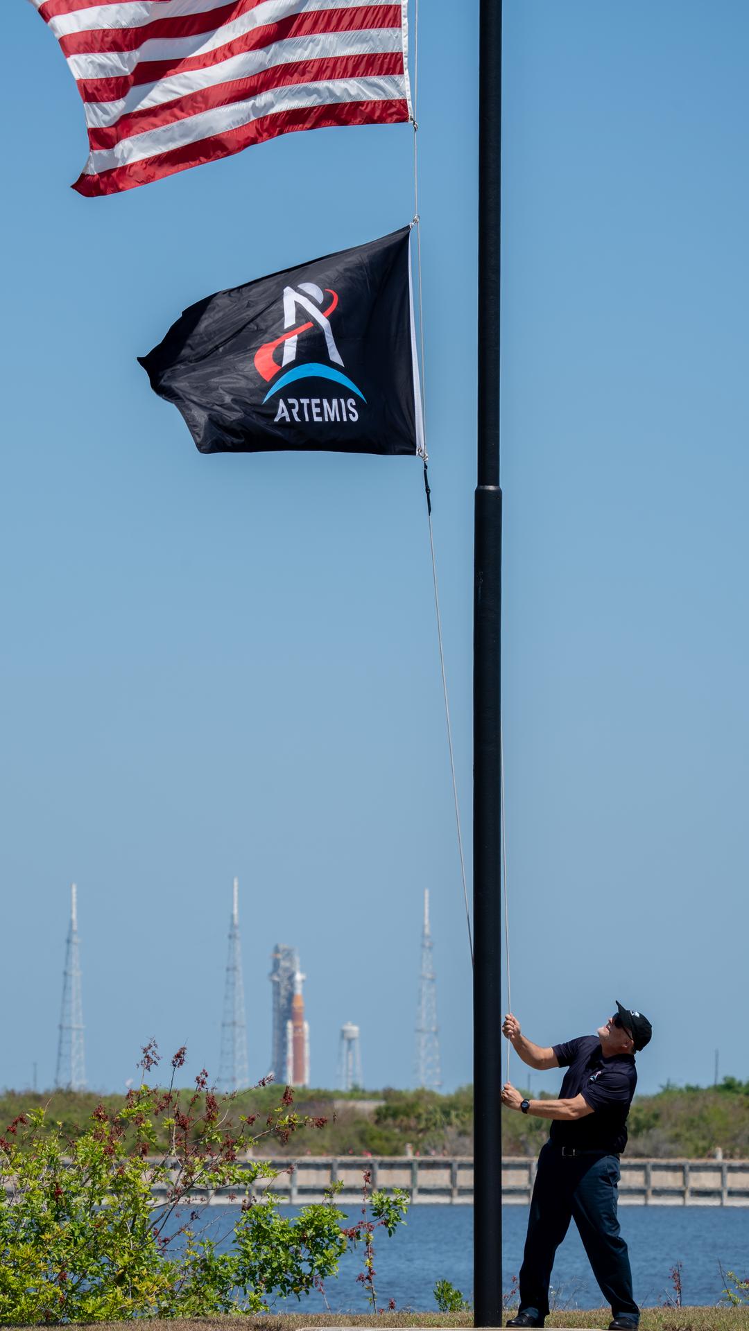 Shawn Quinn, manager, Exploration Ground Systems Program raises the Artemis flag near the countdown clock at the NASA News Center at NASA’s Kennedy Space Center in Florida on Friday, March 27, 2026.  The Artemis II test flight mission will take Artemis II Commander Reid Wiseman, Pilot Victor Glover, and Mission Specialist Christina Koch from NASA, and Mission Specialist Jeremy Hansen from the CSA (Canadian Space Agency) on a 10-day journey around the Moon and back aboard NASA’s SLS (Space Launch System) rocket and Orion spacecraft from Launch Complex 39B no earlier than 6:24 p.m. EDT on Wednesday, April 1. 
