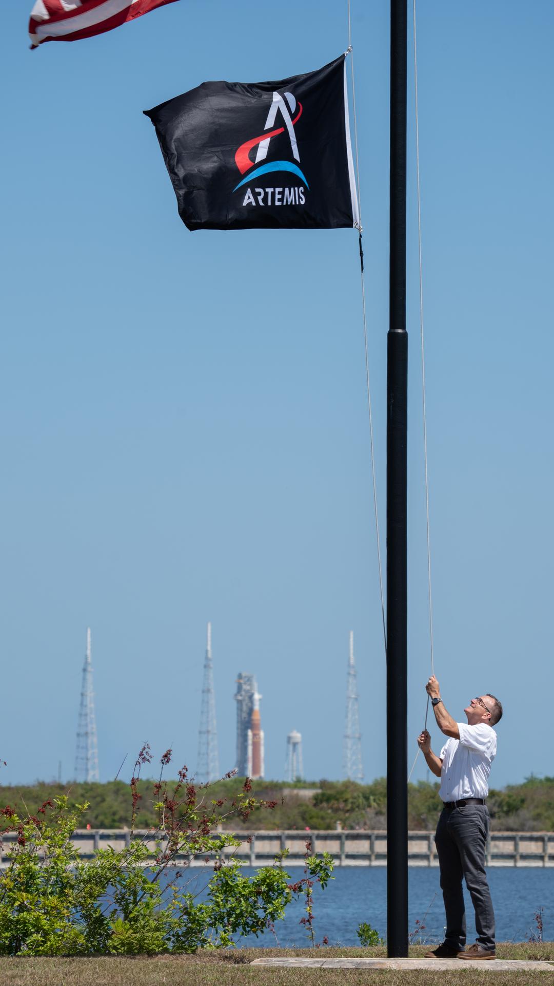 Cliff Lanham, deputy manager, Exploration Ground Systems Program raises the Artemis flag near the countdown clock at the NASA News Center at NASA’s Kennedy Space Center in Florida on Friday, March 27, 2026.  The Artemis II test flight mission will take Artemis II Commander Reid Wiseman, Pilot Victor Glover, and Mission Specialist Christina Koch from NASA, and Mission Specialist Jeremy Hansen from the CSA (Canadian Space Agency) on a 10-day journey around the Moon and back aboard NASA’s SLS (Space Launch System) rocket and Orion spacecraft from Launch Complex 39B no earlier than 6:24 p.m. EDT on Wednesday, April 1. 