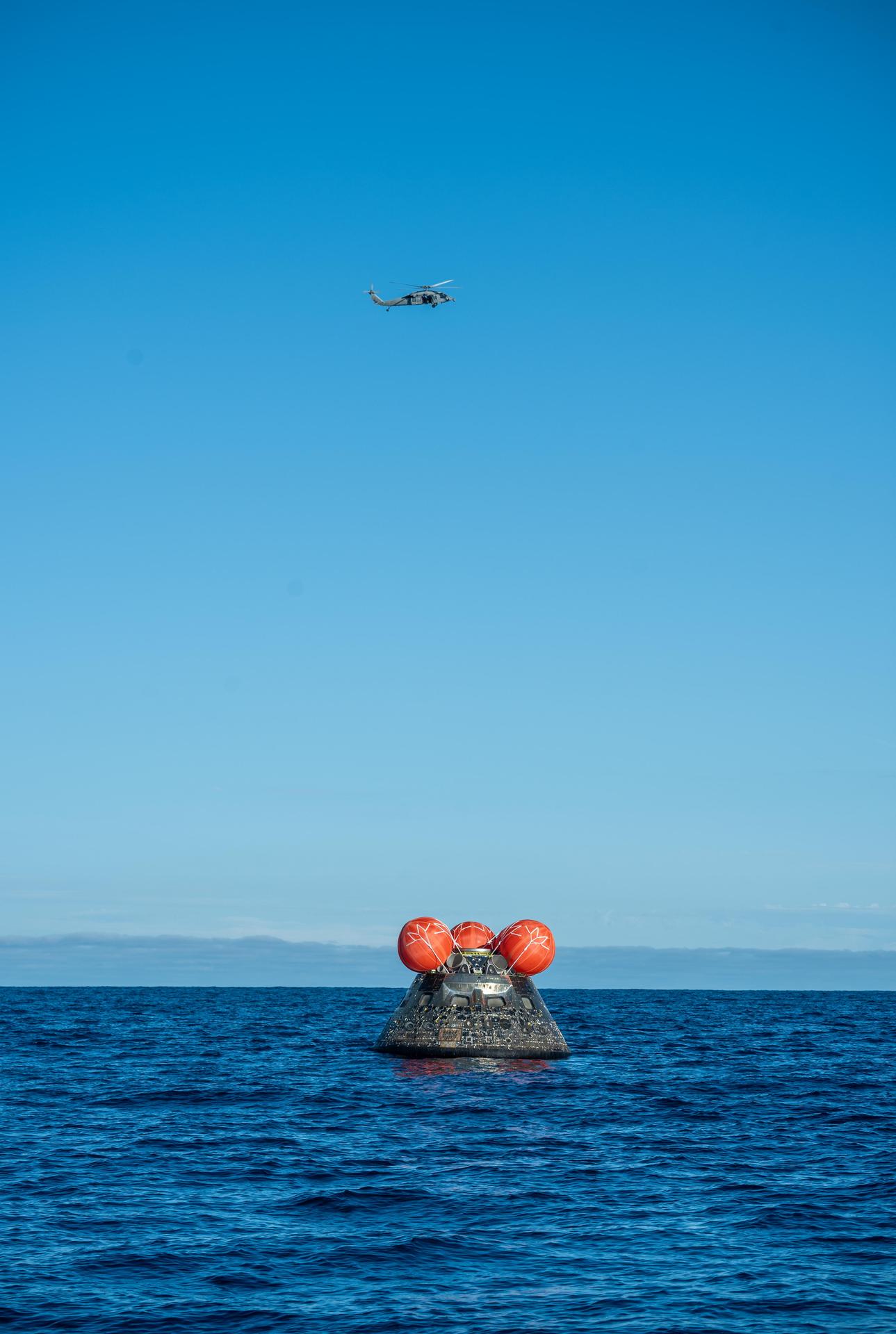 NASA's Orion spacecraft carrying Artemis II Commander Reid Wiseman, Pilot Victor Glover, and Mission Specialist Christina Koch from NASA, along with Mission Specialist Jeremy Hansen from the CSA (Canadian Space Agency), floats in the Pacific Ocean near San Diego, California, at 5:07 p.m. PDT, (8:07 p.m. EDT) on Friday, April 10, 2026. A H60-S Seahawk helicopter hovers above to observe recovery operations to coordinate efforts to secure the spacecraft in the well deck of the ship. The Artemis II test flight launched on Wednesday, April 1, from NASA’s Kennedy Space Center in Florida to begin its 10-day journey around the Moon for scientific discovery, economic benefits, and to build on our foundation for the first crewed missions to Mars.