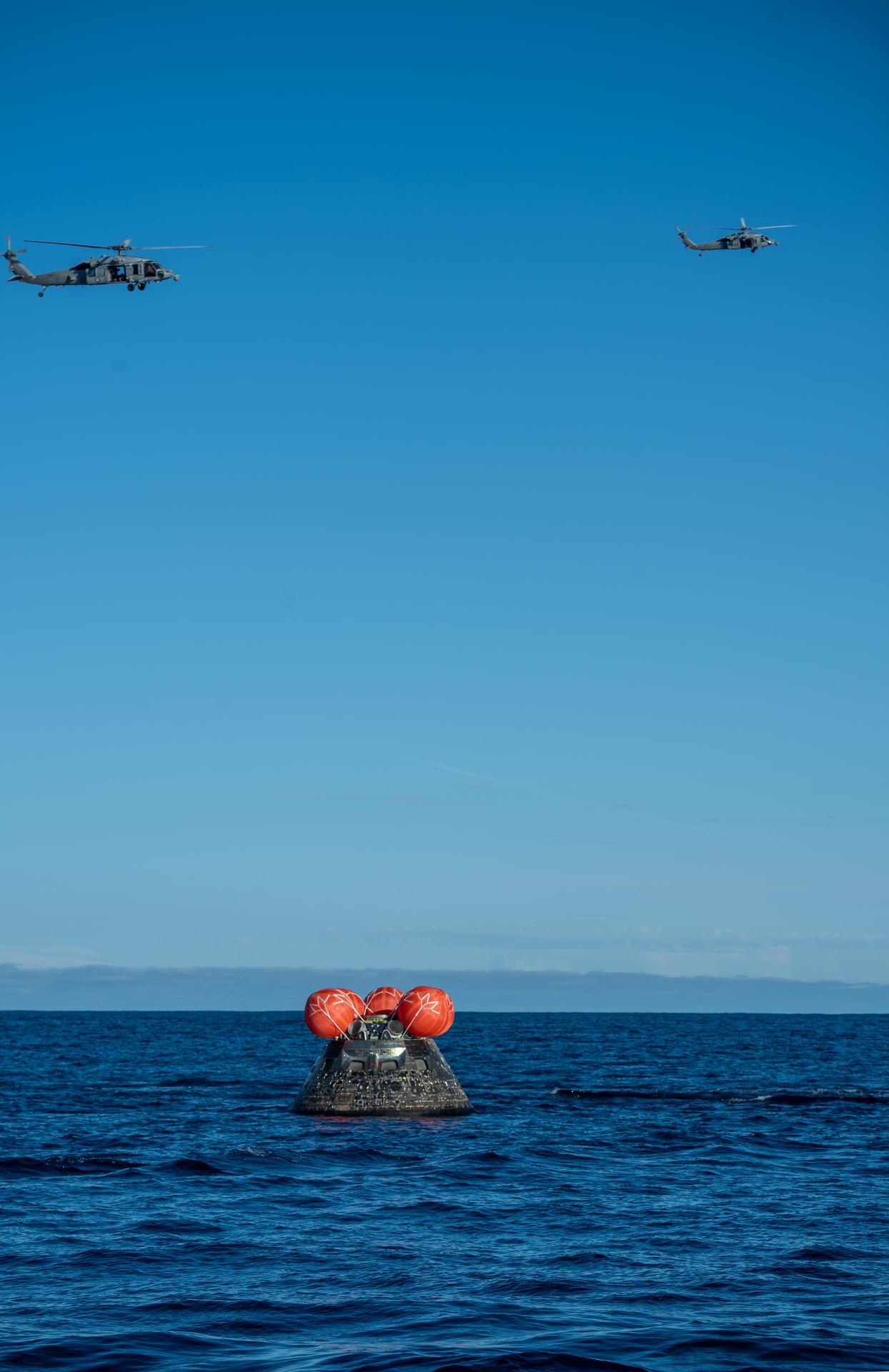 NASA's Orion spacecraft carrying Artemis II Commander Reid Wiseman, Pilot Victor Glover, and Mission Specialist Christina Koch from NASA, along with Mission Specialist Jeremy Hansen from the CSA (Canadian Space Agency), floats in the Pacific Ocean near San Diego, California, at 5:07 p.m. PDT, (8:07 p.m. EDT) on Friday, April 10, 2026. A H60-S Seahawk helicopter hovers above to observe recovery operations to coordinate efforts to secure the spacecraft in the well deck of the ship. The Artemis II test flight launched on Wednesday, April 1, from NASA’s Kennedy Space Center in Florida to begin its 10-day journey around the Moon for scientific discovery, economic benefits, and to build on our foundation for the first crewed missions to Mars.