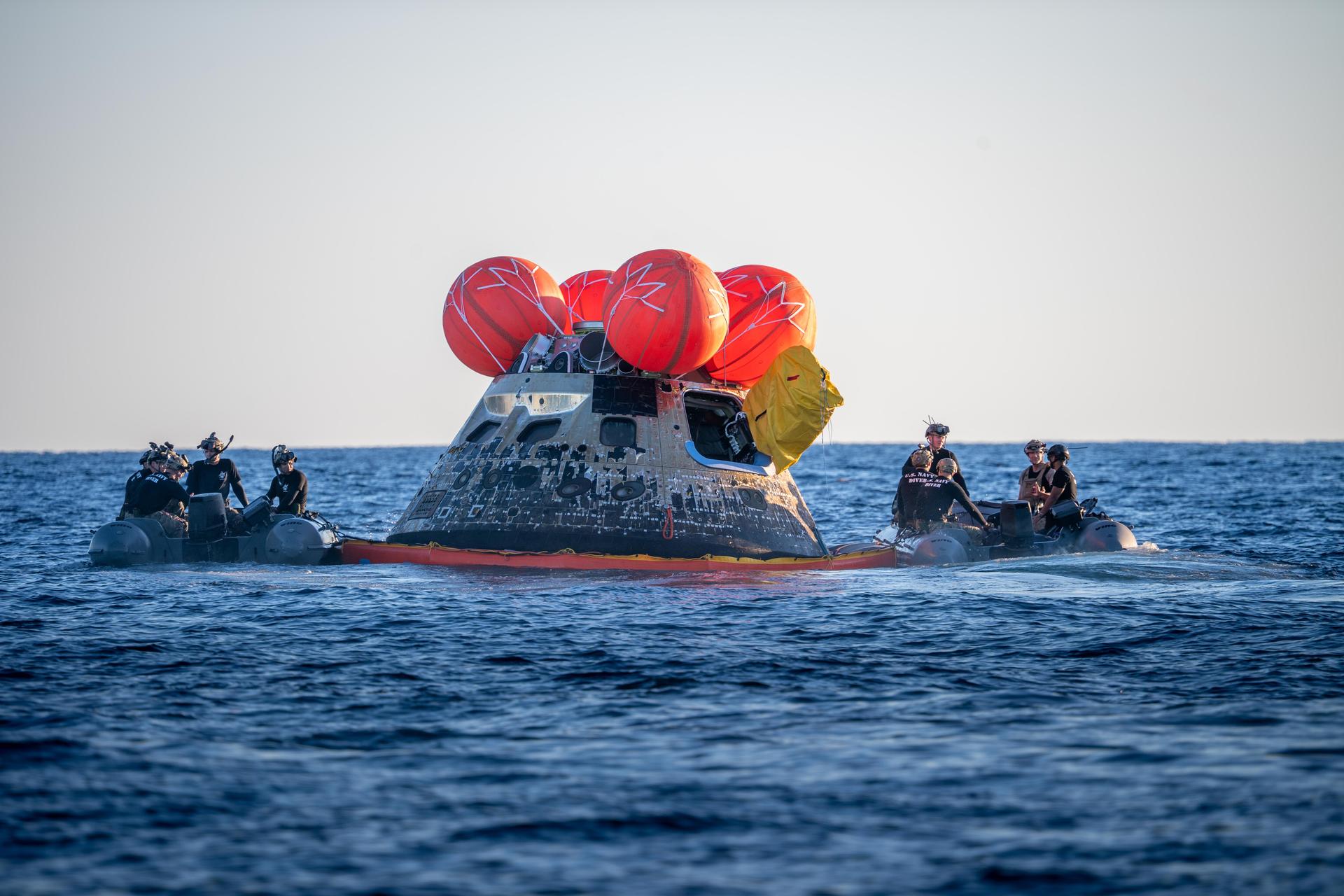U.S. Navy personnel aboard an inflatable raft, called the front porch, help recover NASA's Orion spacecraft following its splashdown in the Pacific Ocean near San Diego, California, at 5:07 p.m. PDT, (8:07 p.m. EDT) on Friday, April 10, 2026, after the Artemis II test flight. The Artemis II mission carrying Artemis II Commander Reid Wiseman, Pilot Victor Glover, and Mission Specialist Christina Koch from NASA, along with Mission Specialist Jeremy Hansen from the CSA (Canadian Space Agency), launched on Wednesday, April 1, from NASA’s Kennedy Space Center in Florida to begin its 10-day journey around the Moon for scientific discovery, economic benefits, and to build on our foundation for the first crewed missions to Mars. NASA’s Landing and Recovery team and the U.S. Navy are coordinating efforts to secure Orion in the well deck of USS John P. Murtha.