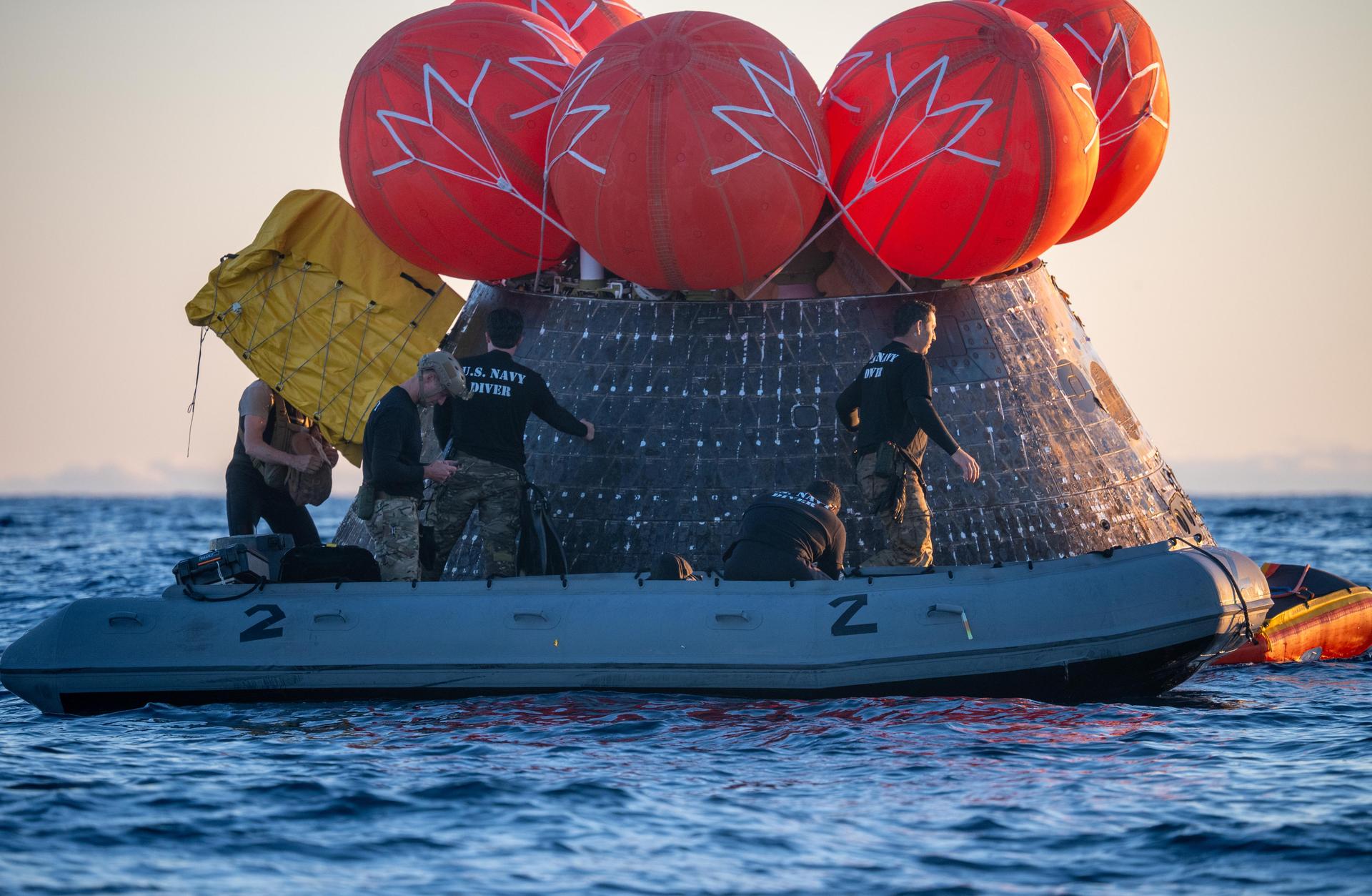U.S. Navy personnel aboard an inflatable raft, called the front porch, help recover NASA's Orion spacecraft following its splashdown in the Pacific Ocean near San Diego, California, at 5:07 p.m. PDT, (8:07 p.m. EDT) on Friday, April 10, 2026, after the Artemis II test flight. The Artemis II mission carrying Artemis II Commander Reid Wiseman, Pilot Victor Glover, and Mission Specialist Christina Koch from NASA, along with Mission Specialist Jeremy Hansen from the CSA (Canadian Space Agency), launched on Wednesday, April 1, from NASA’s Kennedy Space Center in Florida to begin its 10-day journey around the Moon for scientific discovery, economic benefits, and to build on our foundation for the first crewed missions to Mars. NASA’s Landing and Recovery team and the U.S. Navy are coordinating efforts to secure Orion in the well deck of USS John P. Murtha.