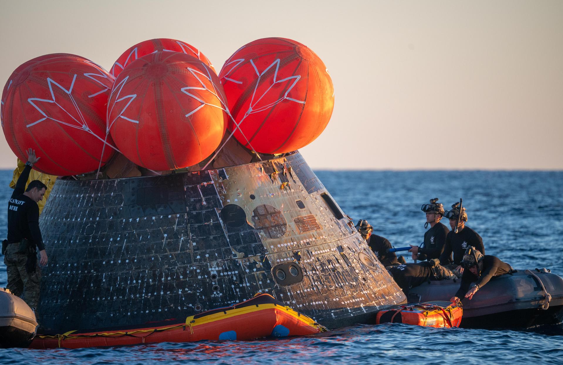U.S. Navy personnel aboard an inflatable raft, called the front porch, help recover NASA's Orion spacecraft following its splashdown in the Pacific Ocean near San Diego, California, at 5:07 p.m. PDT, (8:07 p.m. EDT) on Friday, April 10, 2026, after the Artemis II test flight. The Artemis II mission carrying Artemis II Commander Reid Wiseman, Pilot Victor Glover, and Mission Specialist Christina Koch from NASA, along with Mission Specialist Jeremy Hansen from the CSA (Canadian Space Agency), launched on Wednesday, April 1, from NASA’s Kennedy Space Center in Florida to begin its 10-day journey around the Moon for scientific discovery, economic benefits, and to build on our foundation for the first crewed missions to Mars. NASA’s Landing and Recovery team and the U.S. Navy are coordinating efforts to secure Orion in the well deck of USS John P. Murtha.