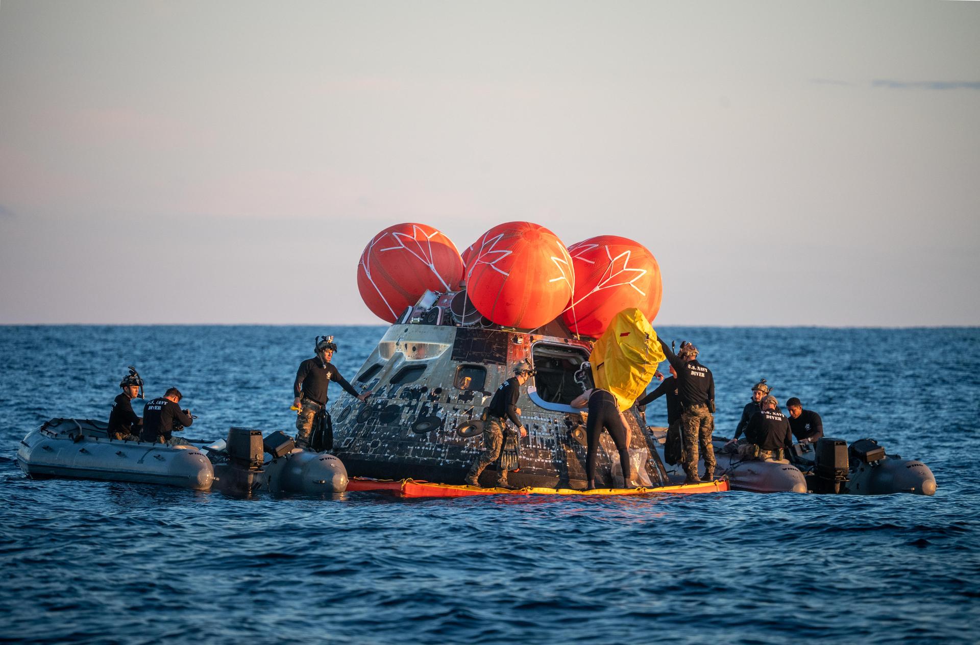 U.S. Navy personnel aboard an inflatable raft, called the front porch, help recover NASA's Orion spacecraft following its splashdown in the Pacific Ocean near San Diego, California, at 5:07 p.m. PDT, (8:07 p.m. EDT) on Friday, April 10, 2026, after the Artemis II test flight. The Artemis II mission carrying Artemis II Commander Reid Wiseman, Pilot Victor Glover, and Mission Specialist Christina Koch from NASA, along with Mission Specialist Jeremy Hansen from the CSA (Canadian Space Agency), launched on Wednesday, April 1, from NASA’s Kennedy Space Center in Florida to begin its 10-day journey around the Moon for scientific discovery, economic benefits, and to build on our foundation for the first crewed missions to Mars. NASA’s Landing and Recovery team and the U.S. Navy are coordinating efforts to secure Orion in the well deck of USS John P. Murtha.