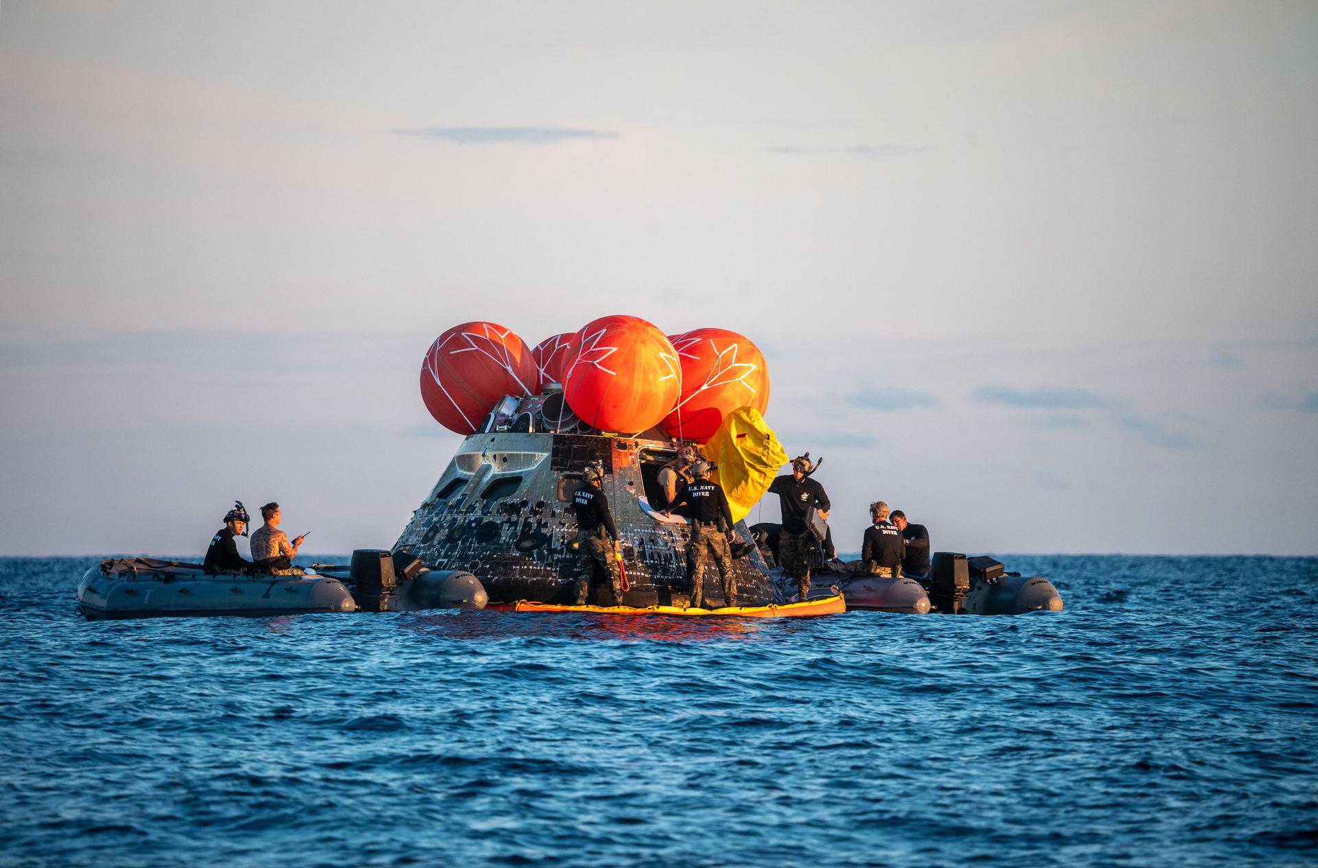U.S. Navy personnel aboard an inflatable raft, called the front porch, help recover NASA's Orion spacecraft following its splashdown in the Pacific Ocean near San Diego, California, at 5:07 p.m. PDT, (8:07 p.m. EDT) on Friday, April 10, 2026, after the Artemis II test flight. The Artemis II mission carrying Artemis II Commander Reid Wiseman, Pilot Victor Glover, and Mission Specialist Christina Koch from NASA, along with Mission Specialist Jeremy Hansen from the CSA (Canadian Space Agency), launched on Wednesday, April 1, from NASA’s Kennedy Space Center in Florida to begin its 10-day journey around the Moon for scientific discovery, economic benefits, and to build on our foundation for the first crewed missions to Mars. NASA’s Landing and Recovery team and the U.S. Navy are coordinating efforts to secure Orion in the well deck of USS John P. Murtha.