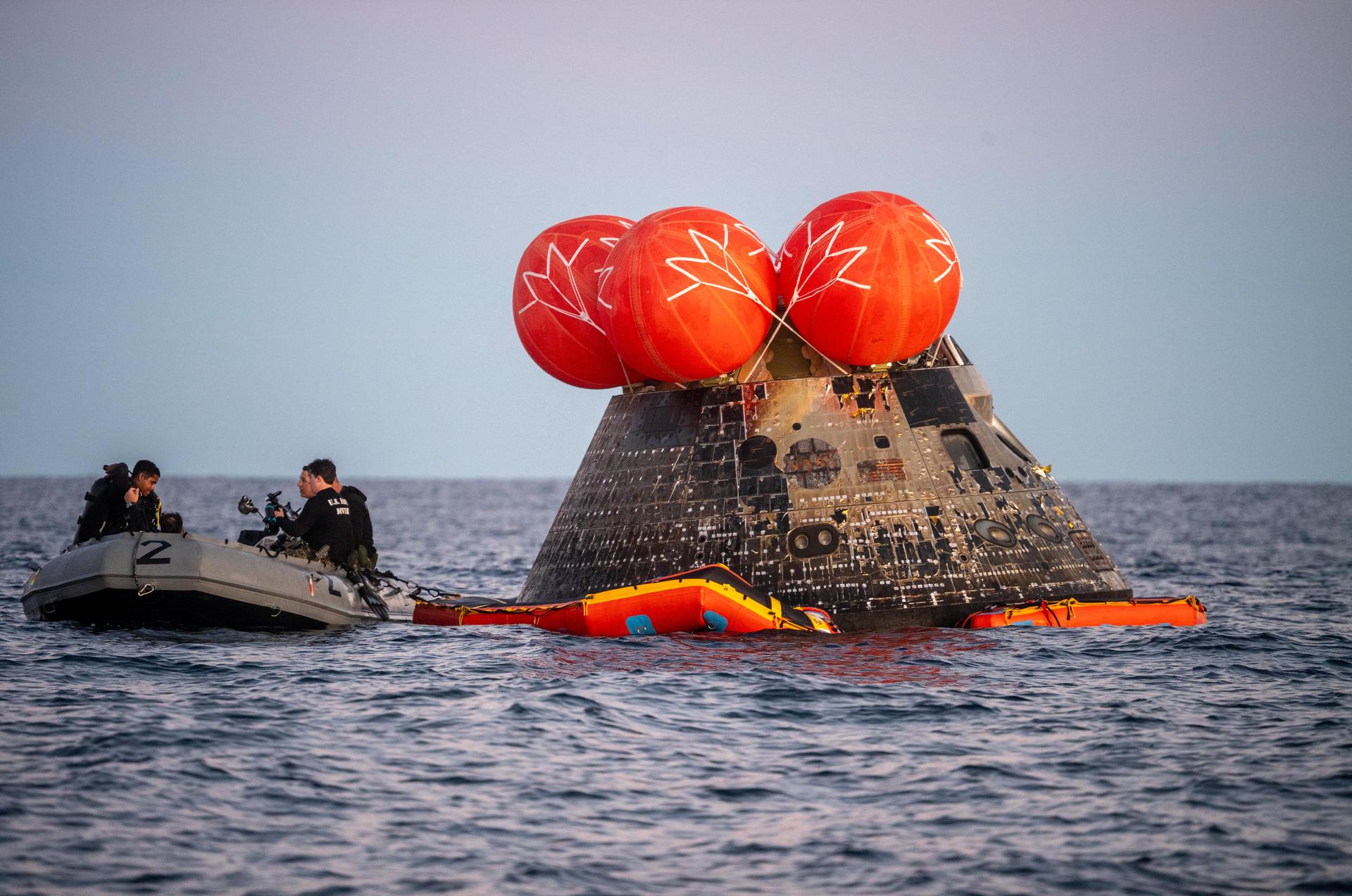 U.S. Navy personnel aboard an inflatable raft help recover NASA's Orion spacecraft following its splashdown in the Pacific Ocean near San Diego, California, at 5:07 p.m. PDT, (8:07 p.m. EDT) on Friday, April 10, 2026, after the Artemis II test flight. The Artemis II mission carrying Artemis II Commander Reid Wiseman, Pilot Victor Glover, and Mission Specialist Christina Koch from NASA, along with Mission Specialist Jeremy Hansen from the CSA (Canadian Space Agency), launched on Wednesday, April 1, from NASA’s Kennedy Space Center in Florida to begin its 10-day journey around the Moon for scientific discovery, economic benefits, and to build on our foundation for the first crewed missions to Mars. NASA’s Landing and Recovery team and the U.S. Navy are coordinating efforts to secure Orion in the well deck of USS John P. Murtha.