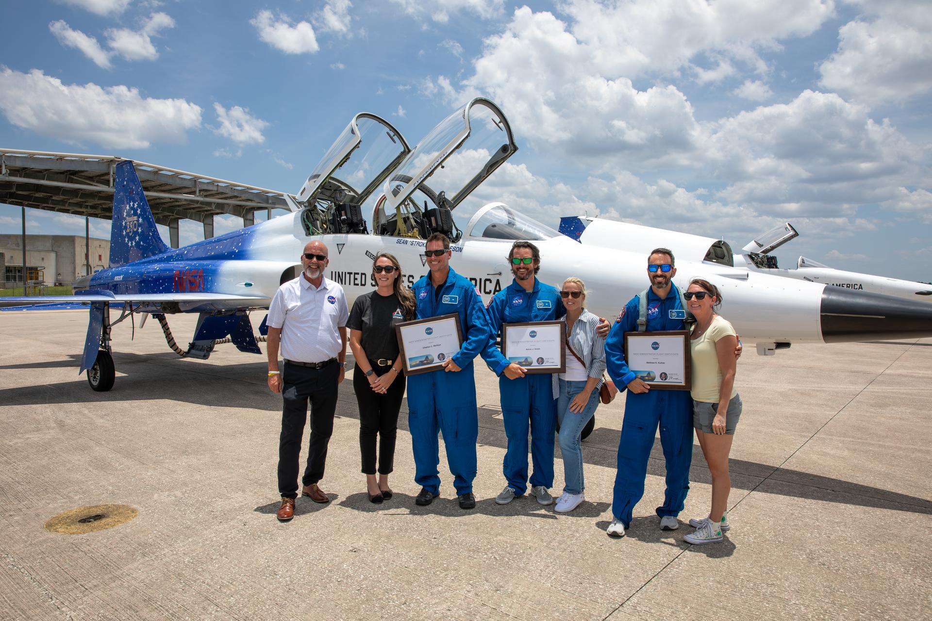 As part of NASA Administrator Jared Isaacman’s Flight Experience Award program and dressed in blue flight suits next to family members, NASA employees Charles Meilbye, Aaron Smith, and Matthew Kufner receive awards from NASA Kennedy’s Director of Human Capital Office, Mike Beaupre (far left), on Wednesday, June 17, 2026, at the Launch and Landing Facility at the agency’s Kennedy Space Center in Florida. The awardees suited up in NASA flight suits, completed preflight briefings, and experienced a unique flight aboard the administrator’s personal F-5 aircraft. The ride-along flight experience award program highlights NASA’s commitment to celebrating excellence across the workforce.