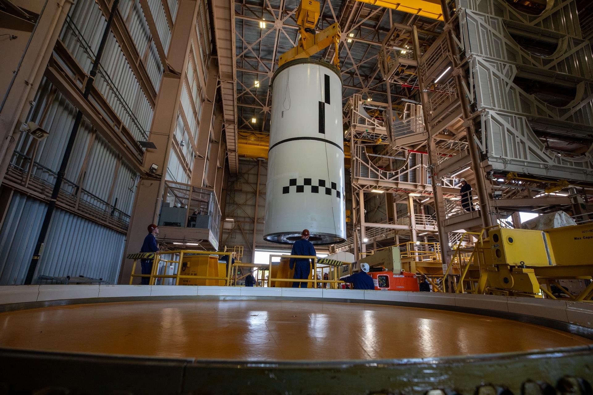 Technicians use a massive crane to lift the right-hand forward center assembly solid rocket booster segment for the Artemis III SLS (Space Launch System) rocket inside the Rotation, Processing, and Surge Facility at NASA’s Kennedy Space Center in Florida on Tuesday, July 14, 2026. The twin boosters, manufactured by Northrop Grumman in Utah, will provide more than 75 percent of the SLS rocket’s total thrust at launch. The Artemis III mission will launch astronauts in the Orion spacecraft on top of the SLS rocket to test rendezvous and docking capabilities between Orion and commercial spacecraft needed to land astronauts on the Moon.