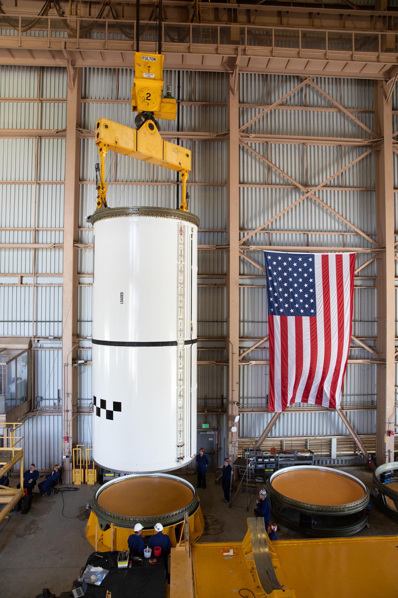 Technicians use a massive crane to lift the right-hand forward center assembly solid rocket booster segment for the Artemis III SLS (Space Launch System) rocket inside the Rotation, Processing, and Surge Facility at NASA’s Kennedy Space Center in Florida on Tuesday, July 14, 2026. The twin boosters, manufactured by Northrop Grumman in Utah, will provide more than 75 percent of the SLS rocket’s total thrust at launch. The Artemis III mission will launch astronauts in the Orion spacecraft on top of the SLS rocket to test rendezvous and docking capabilities between Orion and commercial spacecraft needed to land astronauts on the Moon.