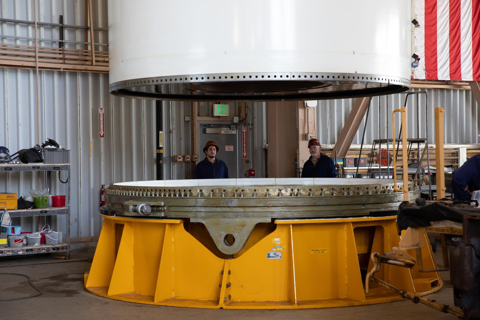 From left, COMET (Consolidated Operations, Management, Engineering, and Test) employees Corbin Nappi, quality assurance inspector, and Terry Williams, engineering technician, monitor the right-hand forward center assembly solid rocket booster segment for the Artemis III SLS (Space Launch System) rocket as it is lowered onto a work stand inside the Rotation, Processing, and Surge Facility at NASA’s Kennedy Space Center in Florida on Tuesday, July 14, 2026. The twin boosters, manufactured by Northrop Grumman in Utah, will provide more than 75 percent of the SLS rocket’s total thrust at launch. The Artemis III mission will launch astronauts in the Orion spacecraft on top of the SLS rocket to test rendezvous and docking capabilities between Orion and commercial spacecraft needed to land astronauts on the Moon.