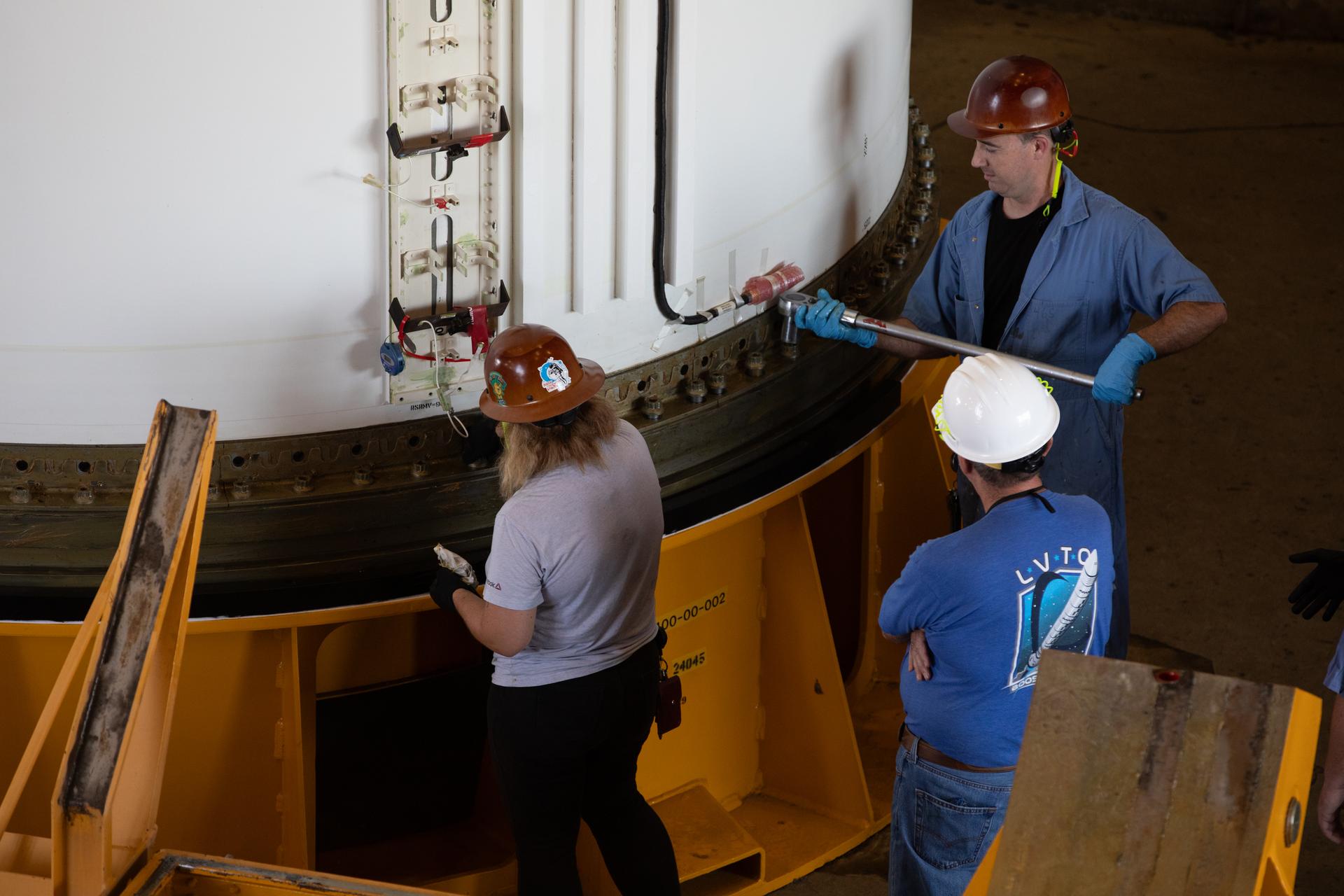 From left, COMET (Consolidated Operations, Management, Engineering, and Test) employees Tia Harbour, engineering technician; Caleb Waters, engineering technician; and Kenny Wright, Booster Element Office representative, monitor the right-hand forward center assembly solid rocket booster segment for the Artemis III SLS (Space Launch System) rocket lowered onto a work stand inside the Rotation, Processing, and Surge Facility at NASA’s Kennedy Space Center in Florida on Tuesday, July 14, 2026. The twin boosters, manufactured by Northrop Grumman in Utah, will provide more than 75 percent of the SLS rocket’s total thrust at launch. The Artemis III mission will launch astronauts in the Orion spacecraft on top of the SLS rocket to test rendezvous and docking capabilities between Orion and commercial spacecraft needed to land astronauts on the Moon. 