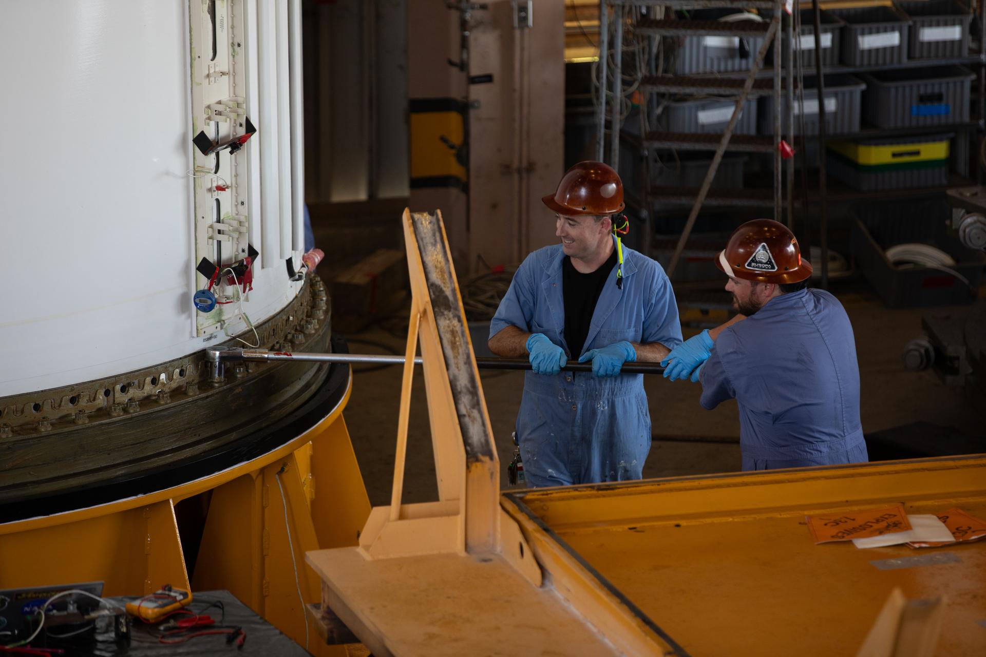 From left, COMET (Consolidated Operations, Management, Engineering, and Test) employees Caleb Waters and Alex Novratil, engineer technicians, secure the right-hand forward center assembly solid rocket booster segment for the Artemis III SLS (Space Launch System) rocket onto a work stand inside the Rotation, Processing, and Surge Facility at NASA’s Kennedy Space Center in Florida on Tuesday, July 14, 2026. The twin boosters, manufactured by Northrop Grumman in Utah, will provide more than 75 percent of the SLS rocket’s total thrust at launch. The Artemis III mission will launch astronauts in the Orion spacecraft on top of the SLS rocket to test rendezvous and docking capabilities between Orion and commercial spacecraft needed to land astronauts on the Moon. 