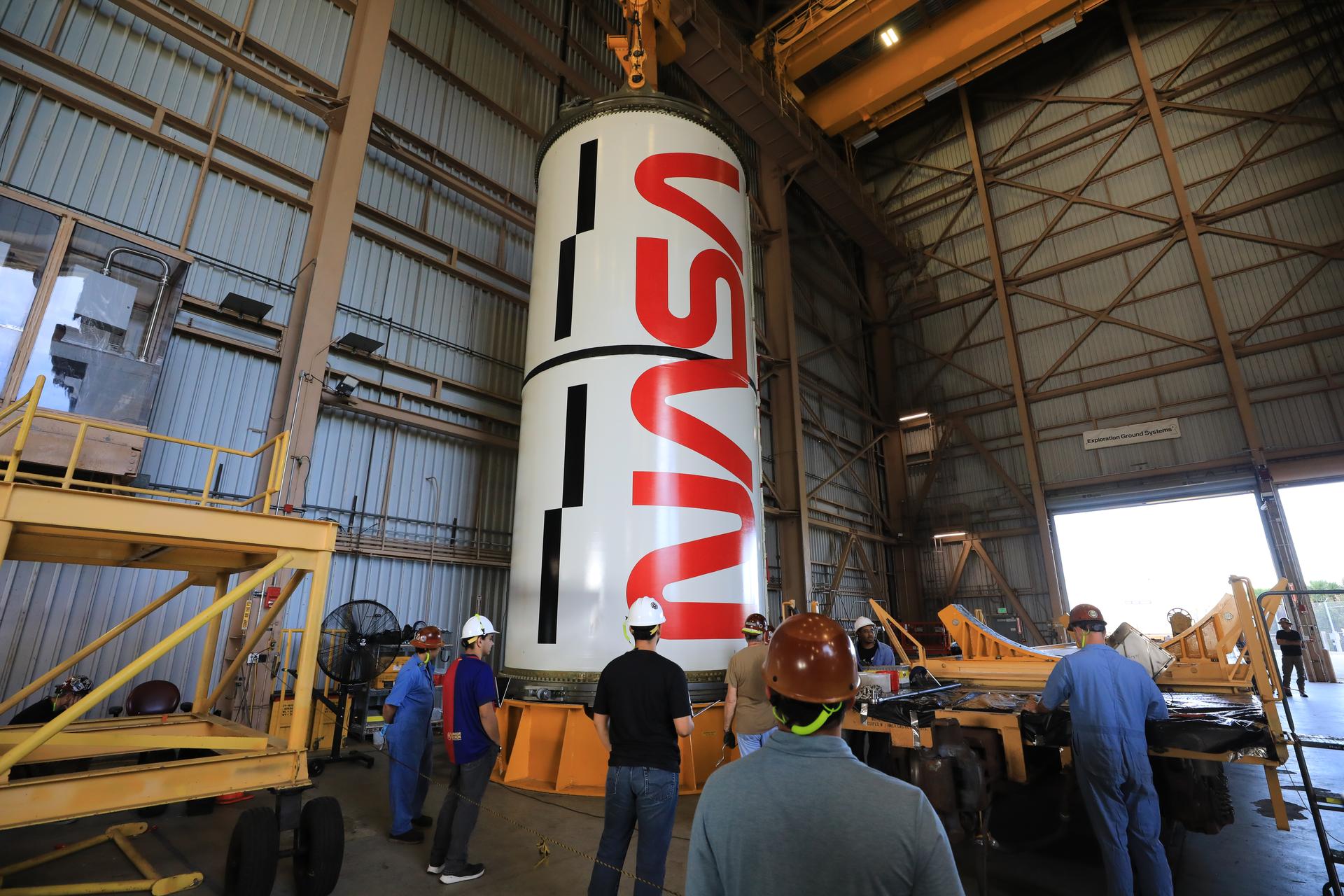 Technicians with NASA’s Exploration Ground Systems Program lift the right center center solid rocket booster, containing the NASA “worm” insignia, for the agency’s Artemis III SLS (Space Launch System) rocket onto the work stand ahead of inspection inside the Rotation, Processing and Surge Facility at the agency’s Kennedy Space Center in Florida on Wednesday, July 22, 2026. The SLS rocket’s twin boosters, manufactured by Northrop Grumman in Utah, will provide more than 75 percent of the SLS rocket’s total thrust at launch. The Artemis III mission will launch crew in the Orion spacecraft on top of the SLS rocket to test rendezvous and docking capabilities between Orion and commercial spacecraft needed to land astronauts on the Moon.