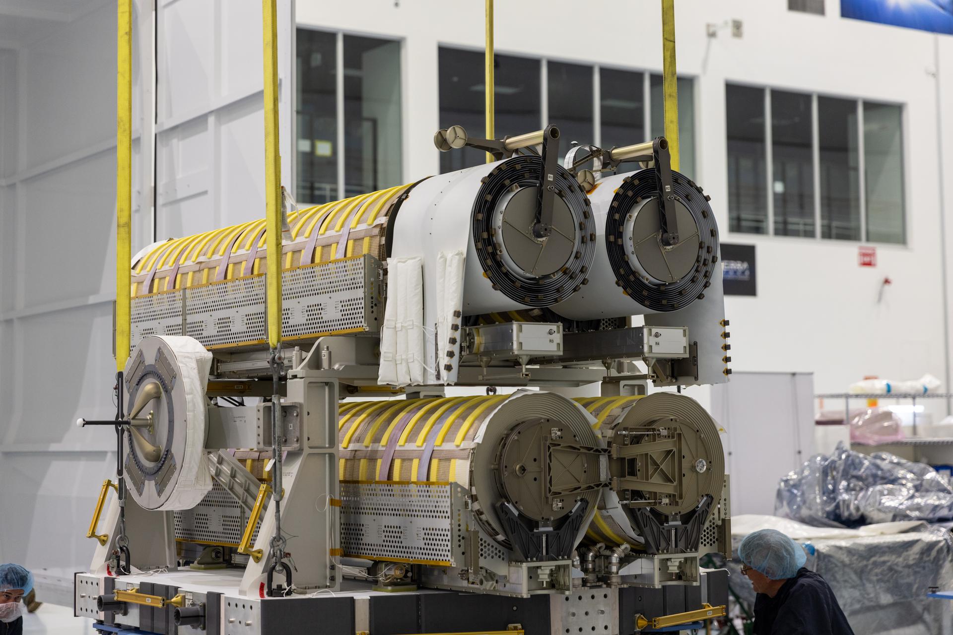 Technicians assist a crane to lower a pair of International Space Station Roll Out Solar Arrays (iROSA) onto a platform on Tuesday, Aug. 11, 2026, inside the Space Systems Processing Facility at NASA’s Kennedy Space Center in Florida. The iROSA are being prepared for delivery to the space station aboard SpaceX’s Dragon cargo carrier on the company’s 35th commercial resupply services (CRS-35) mission to the space station. iROSA is a new generation of solar arrays that roll open in space and is more compact than previous arrays while providing the same amount of power. With six similar arrays already in place on the station, the final pair will complete the power system upgrade for the orbiting laboratory.