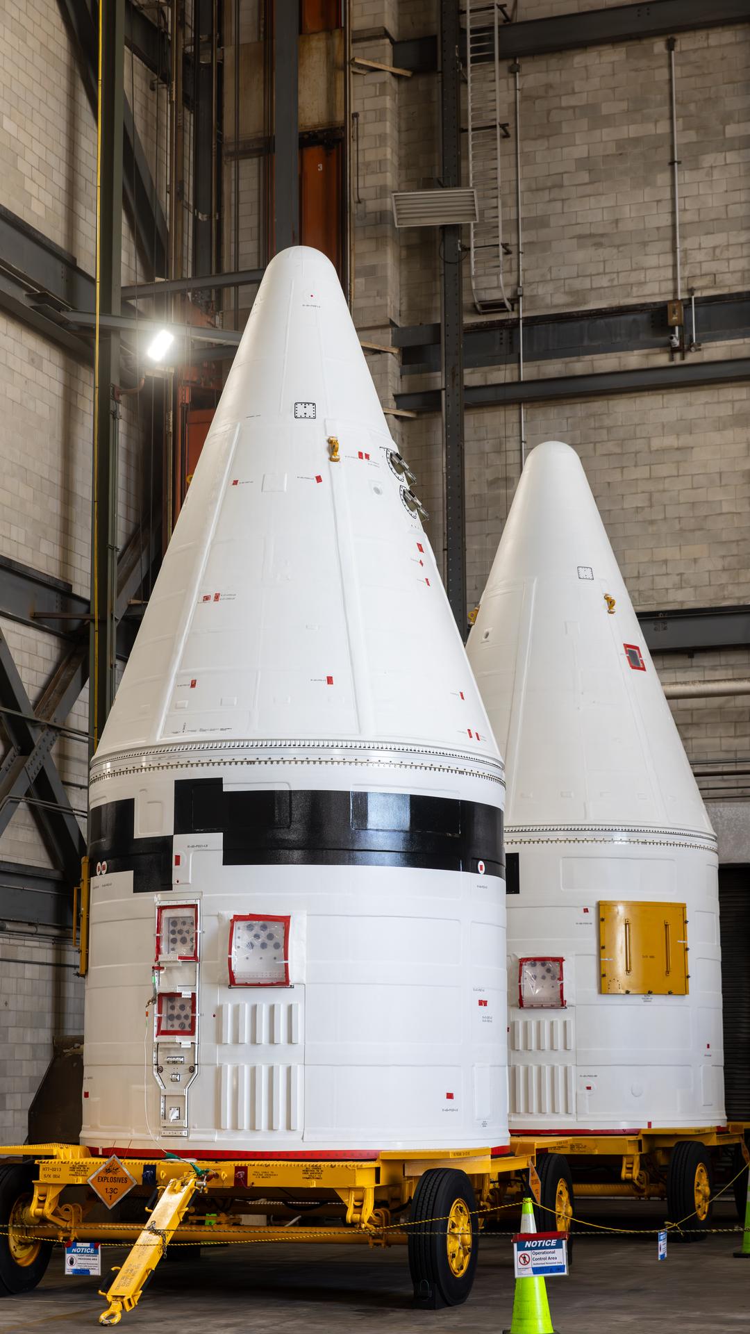 The left, with black stripe, and right aerodynamic forward assemblies for the twin SLS (Space Launch System) solid rocket boosters for Artemis III arrive at the Vehicle Assembly Building at NASA’s Kennedy Space Center in Florida on Thursday, Aug. 13, 2026. The nose cones will be integrated atop the SLS boosters to provide a smooth, pointed shape that allows the boosters to cut through the atmosphere efficiently, reducing drag and keeping the rocket stable during ascent. Artemis III will carry out a series of objectives in low Earth orbit designed to demonstrate critical systems needed for future lunar landings, beginning with Artemis IV.  