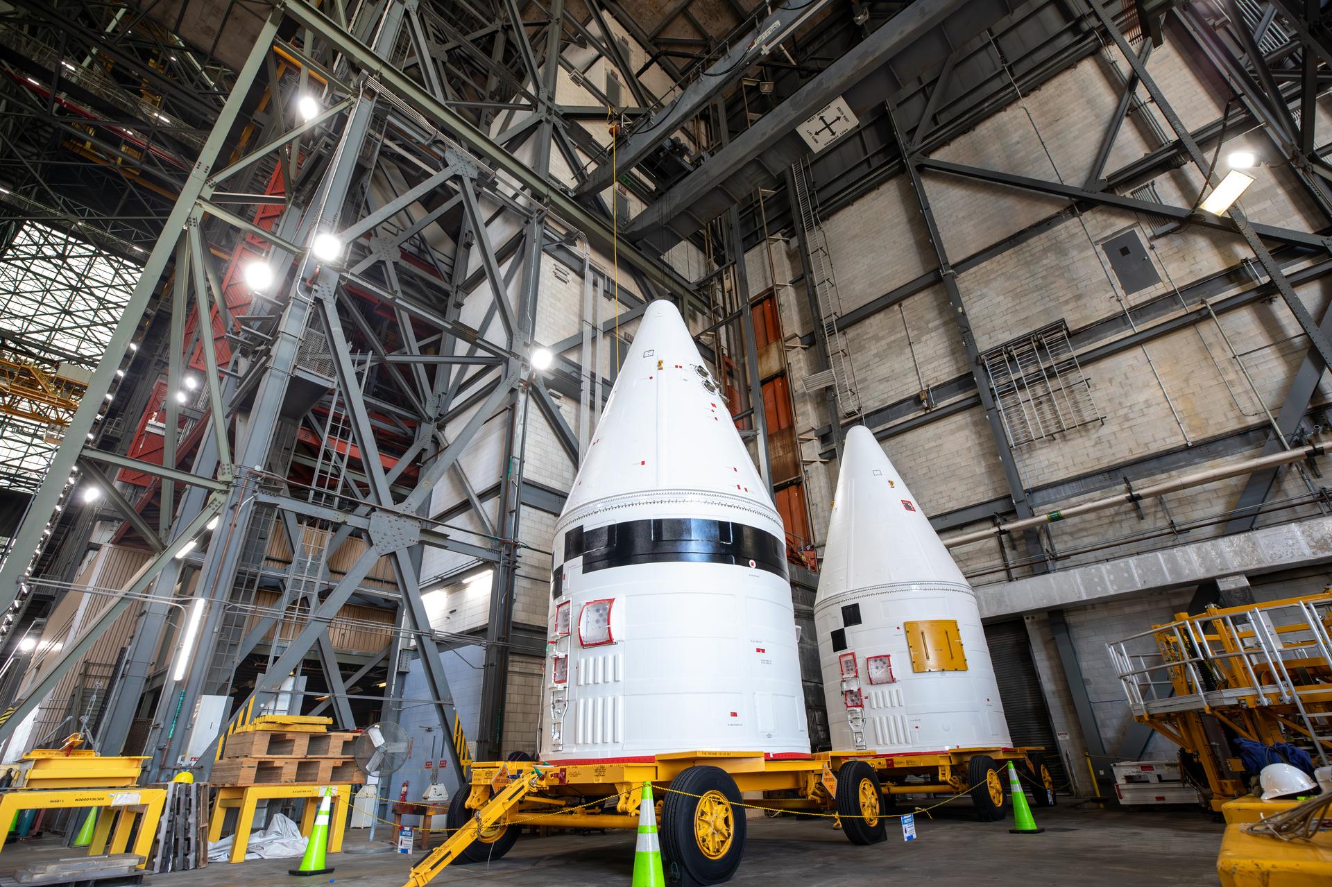 The left, with black stripe, and right aerodynamic forward assemblies for the twin SLS (Space Launch System) solid rocket boosters for Artemis III arrive at the Vehicle Assembly Building at NASA’s Kennedy Space Center in Florida on Thursday, Aug. 13, 2026. The nose cones will be integrated atop the SLS boosters to provide a smooth, pointed shape that allows the boosters to cut through the atmosphere efficiently, reducing drag and keeping the rocket stable during ascent. Artemis III will carry out a series of objectives in low Earth orbit designed to demonstrate critical systems needed for future lunar landings, beginning with Artemis IV.  