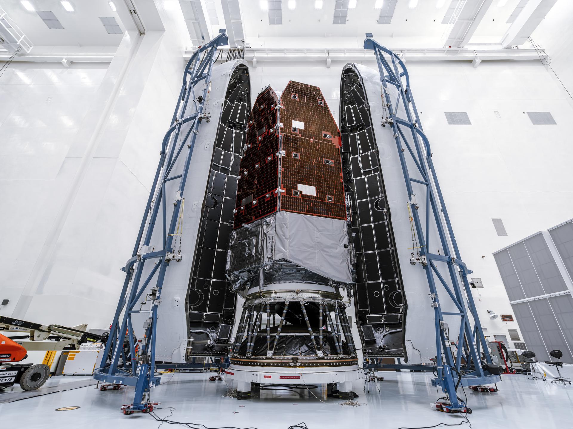 Full-height view of the Roman Space Telescope inside the tall payload fairing. Blue support structures stand on each side in the cleanroom environment.