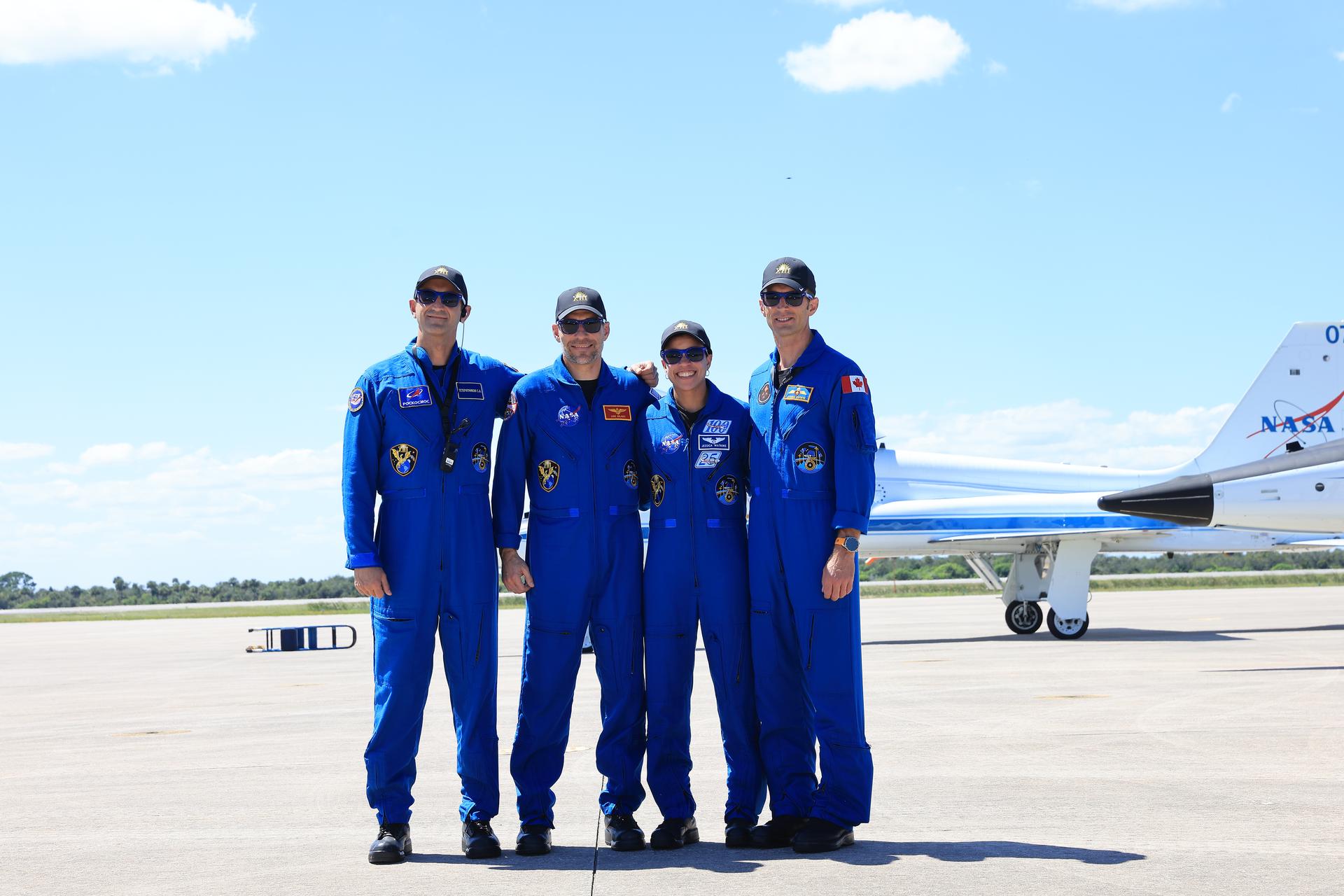 Astronauts in blue flight suits stand on the runway of Kennedy Space Center's Shuttle Landing Facility during a media event. 
