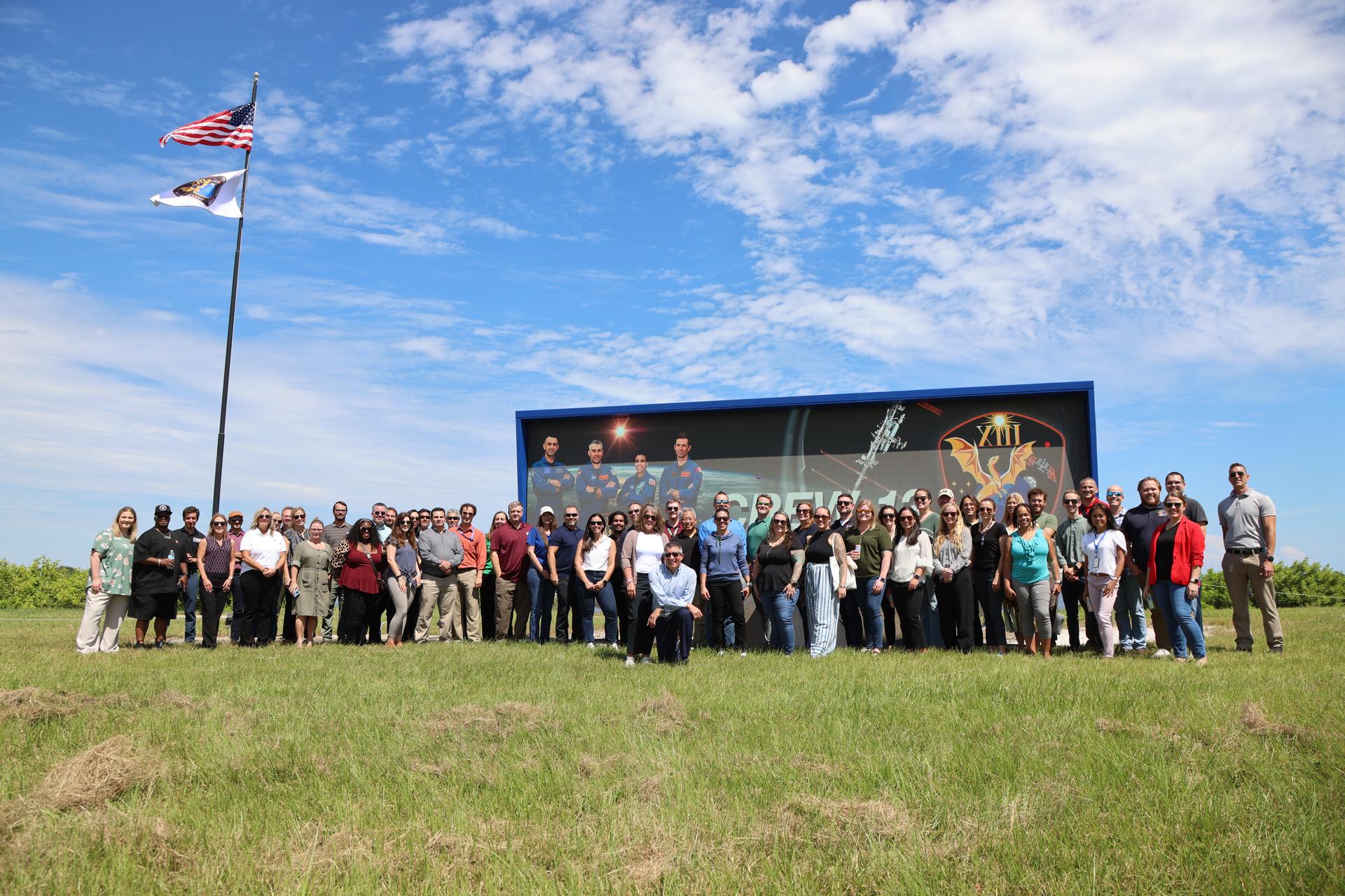 Members of  NASA's Commercial Crew Office within the Low Earth Orbit Program pose for a photograph with the agency’s SpaceX Crew-13 mission flag near the countdown clock at the NASA News Center at the agency’s Kennedy Space Center in Florida on Tuesday, Sept. 29, 2026. The Crew-13 mission will send NASA astronauts Jessica Watkins and Luke Delaney, CSA (Canadian Space Agency) astronaut Joshua Kutryk, and Roscosmos cosmonaut Sergey Teteryatnikov to the International Space Station aboard SpaceX’s Dragon spacecraft and Falcon 9 rocket at 11:10 a.m. EDT on Thursday, Oct. 1, from Cape Canaveral Space Force Station’s Space Launch Complex 40.